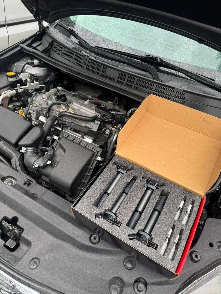 Car engine with a box of spark plugs and ignition coils on the engine bay.