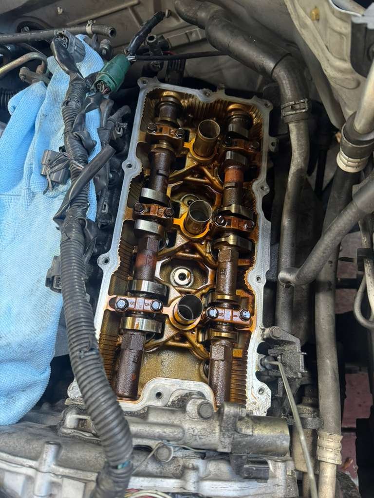 View of a disassembled car engine cylinder head with valve springs, camshafts, and rockers visible.