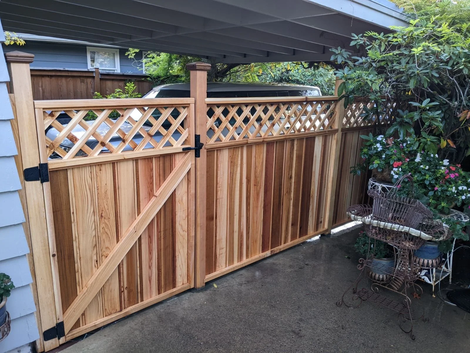 New wooden gate and fence in a backyard, with a small gate and lattice work at the top, and potted plants and outdoor furniture nearby.