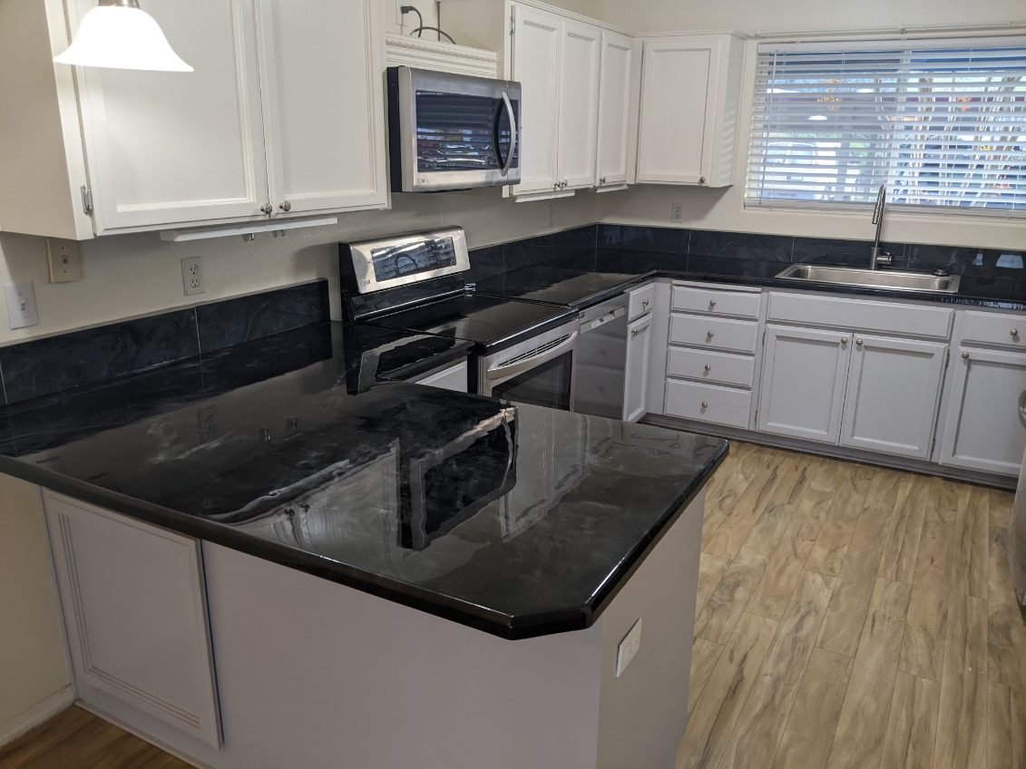 Kitchen with white cabinets, black countertops, stainless steel appliances, and a window above the sink.