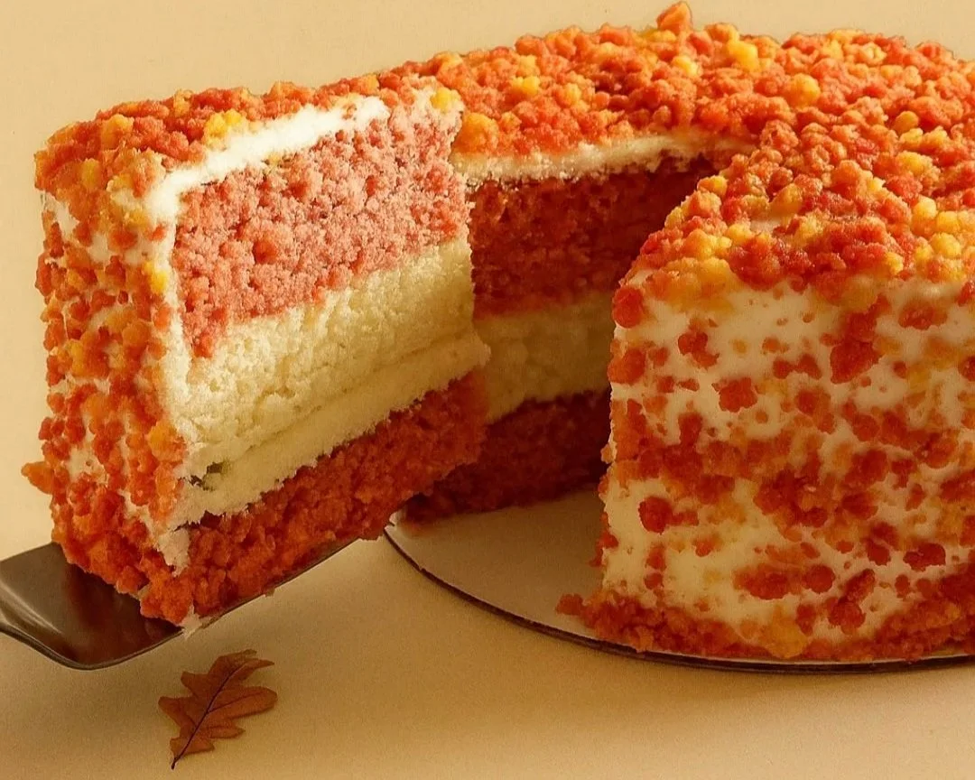 A carrot cake with cream cheese frosting and chopped nuts, partially sliced to reveal layers inside.