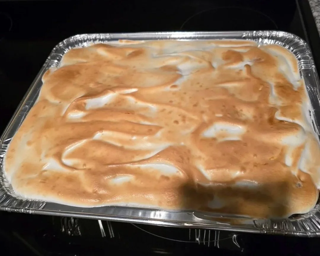 Baked dessert with a light brown and white swirled topping in a disposable aluminum pan.