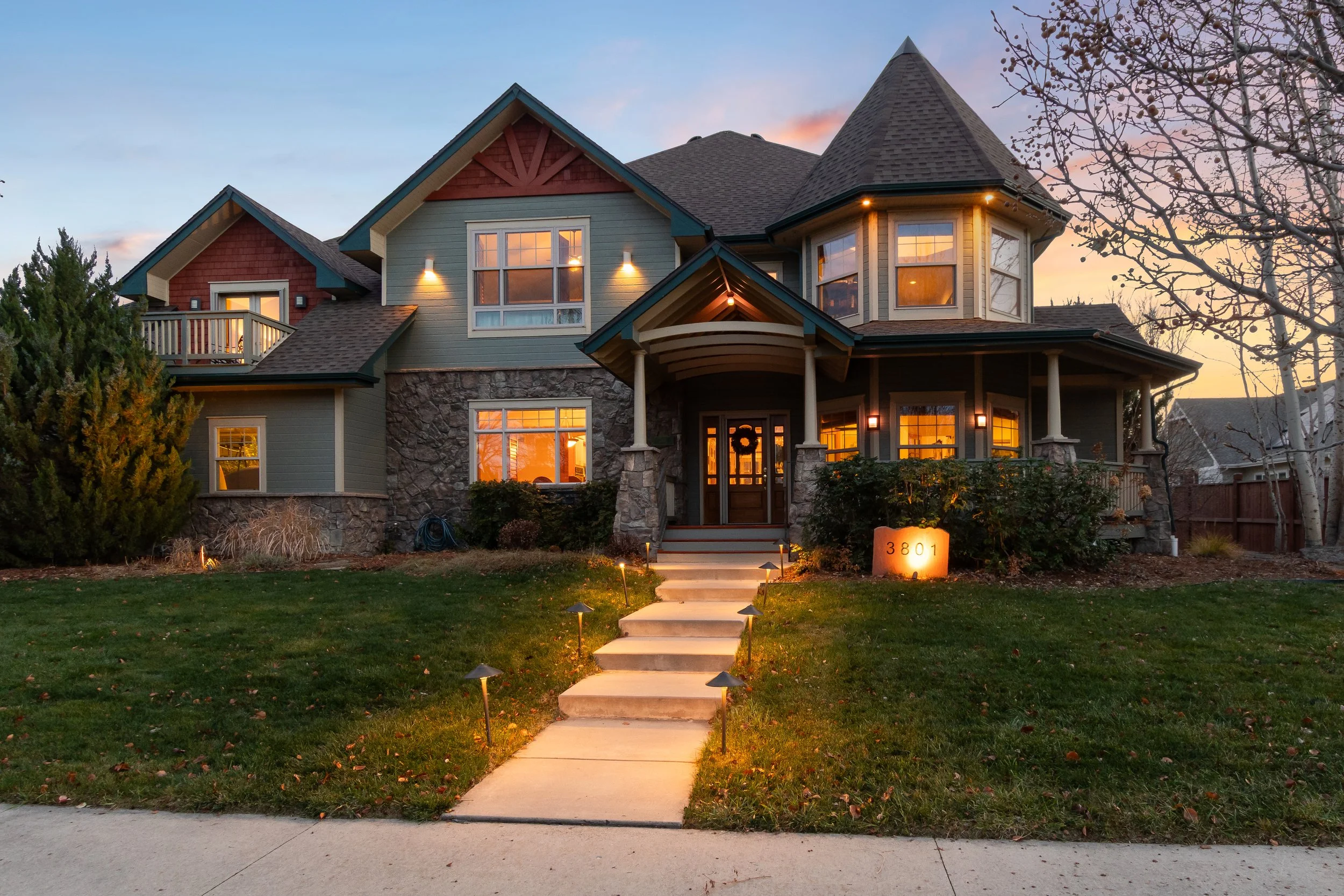 A large, multi-story house Victorian house in McIntosh farms neighborhood. Listed by Logan Schlutz Longmont Realtor. Stone and wooden exterior, covered front porch in craftsman style. Steep roof. Located one minute walk to private trails and Lake.