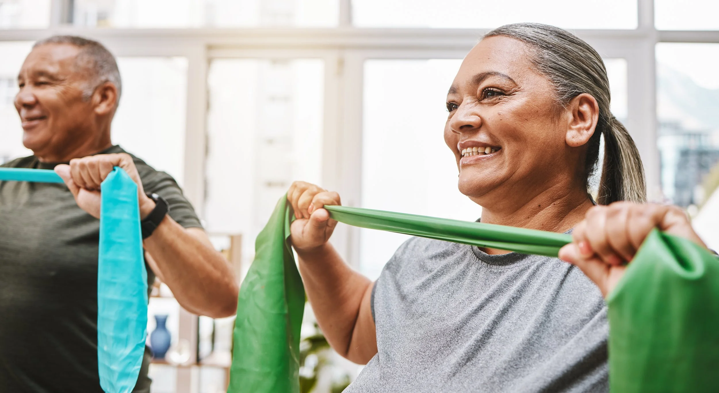 Senior man and woman exercising with resistance bands in a bright gym.