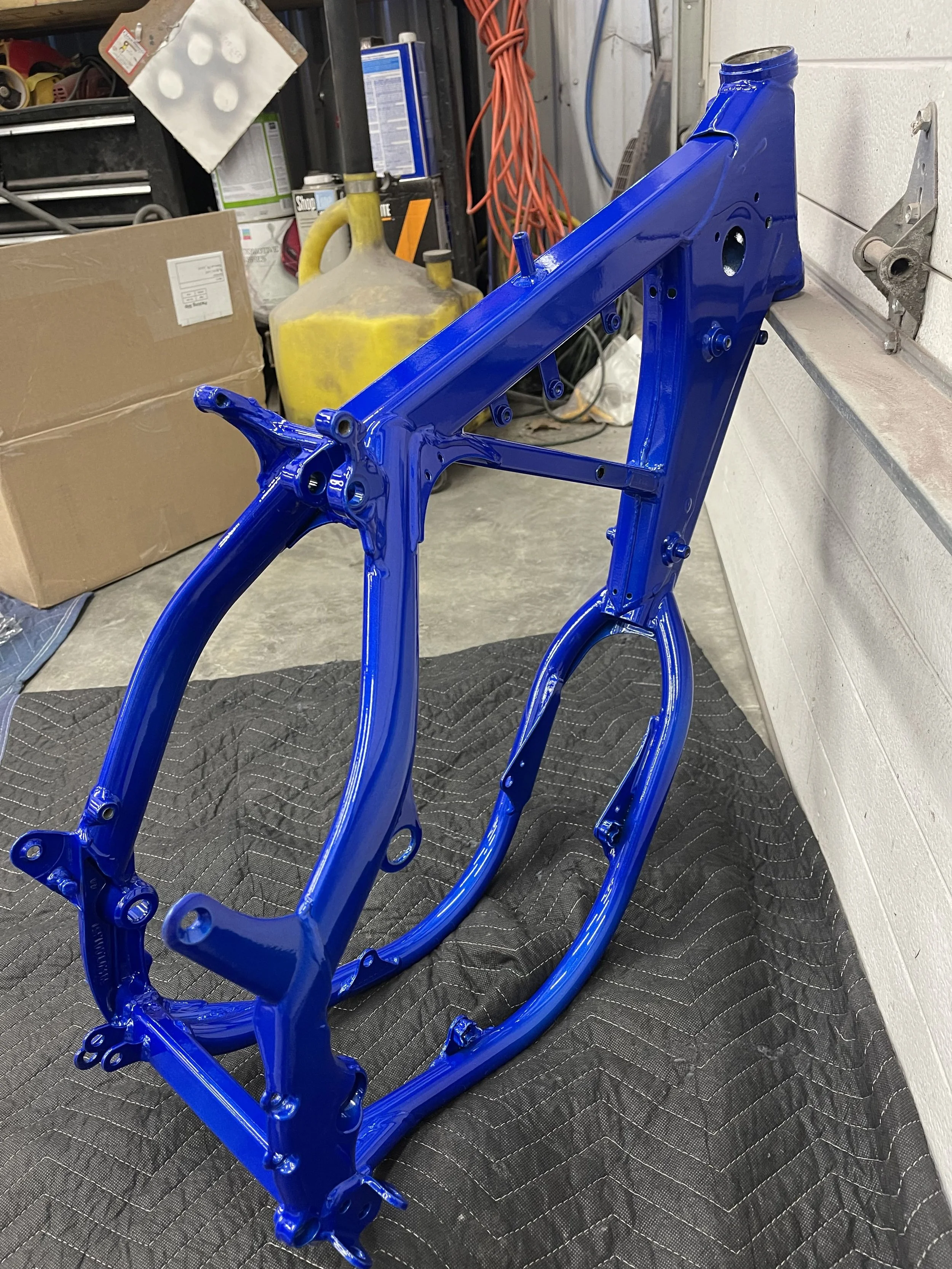 Blue painted bicycle frame on a padded surface in a workshop.