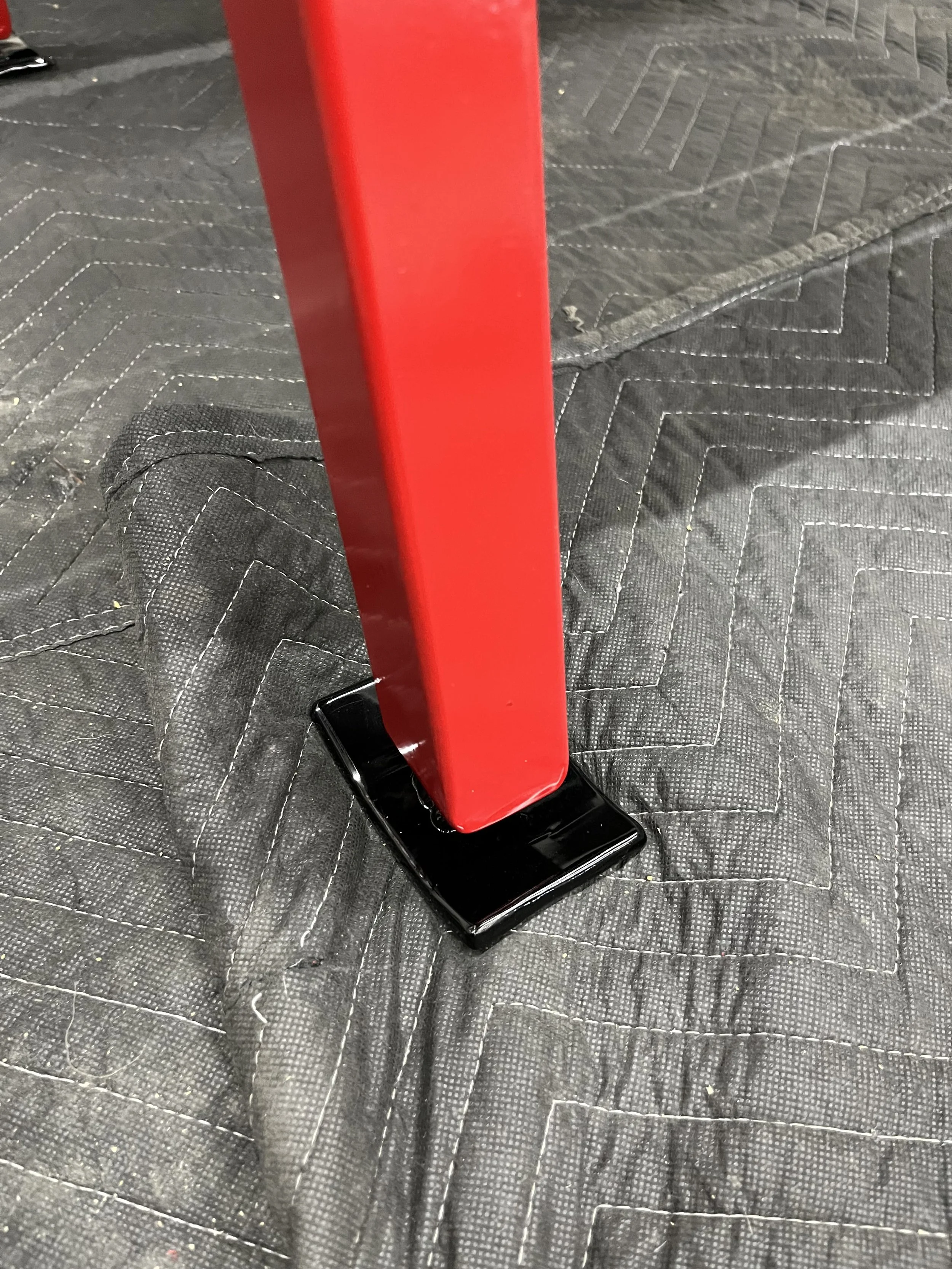 Close-up of a red metal post with a black base on a black quilted surface.