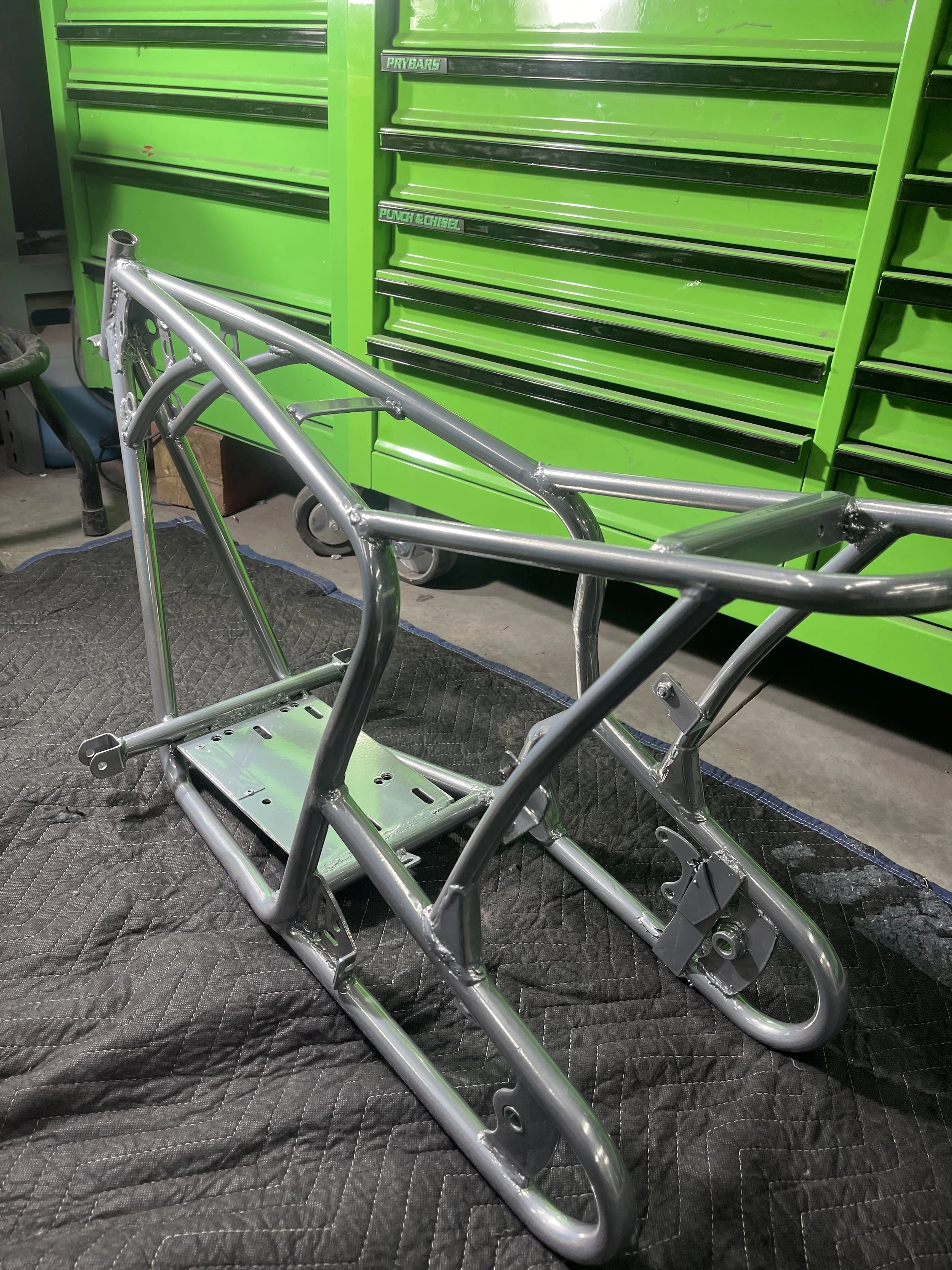Unassembled motorcycle frame in a garage with green tool cabinet in the background.