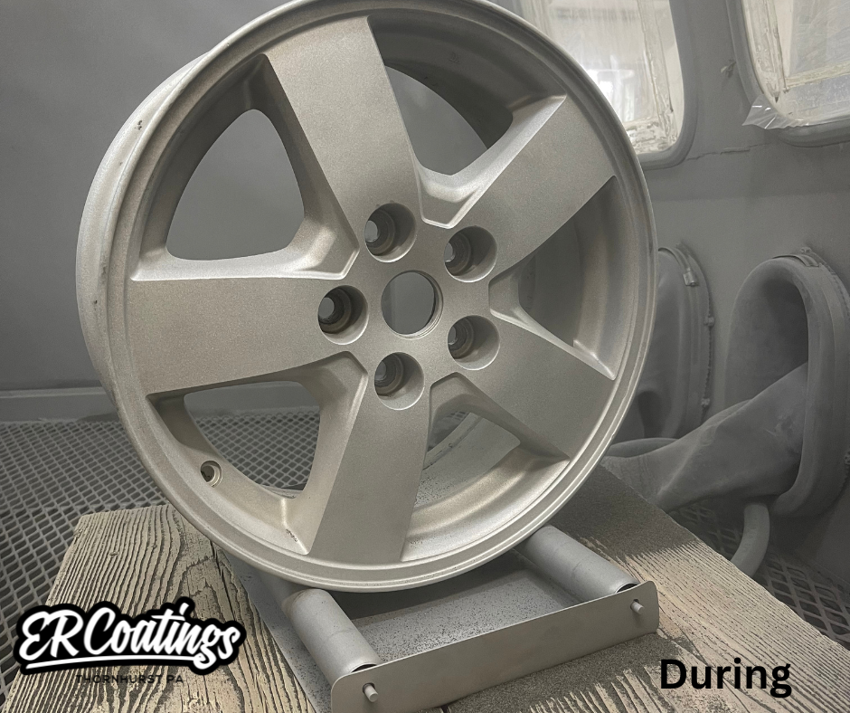 A silver alloy wheel rim on a stand in a spray booth during a coating process.