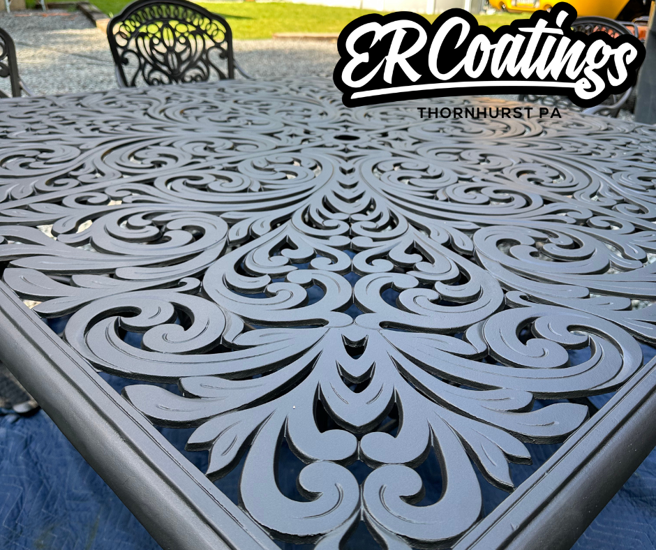 Close-up of an ornate, decorative metal table with intricate scrolling patterns, outdoors with chairs in the background.