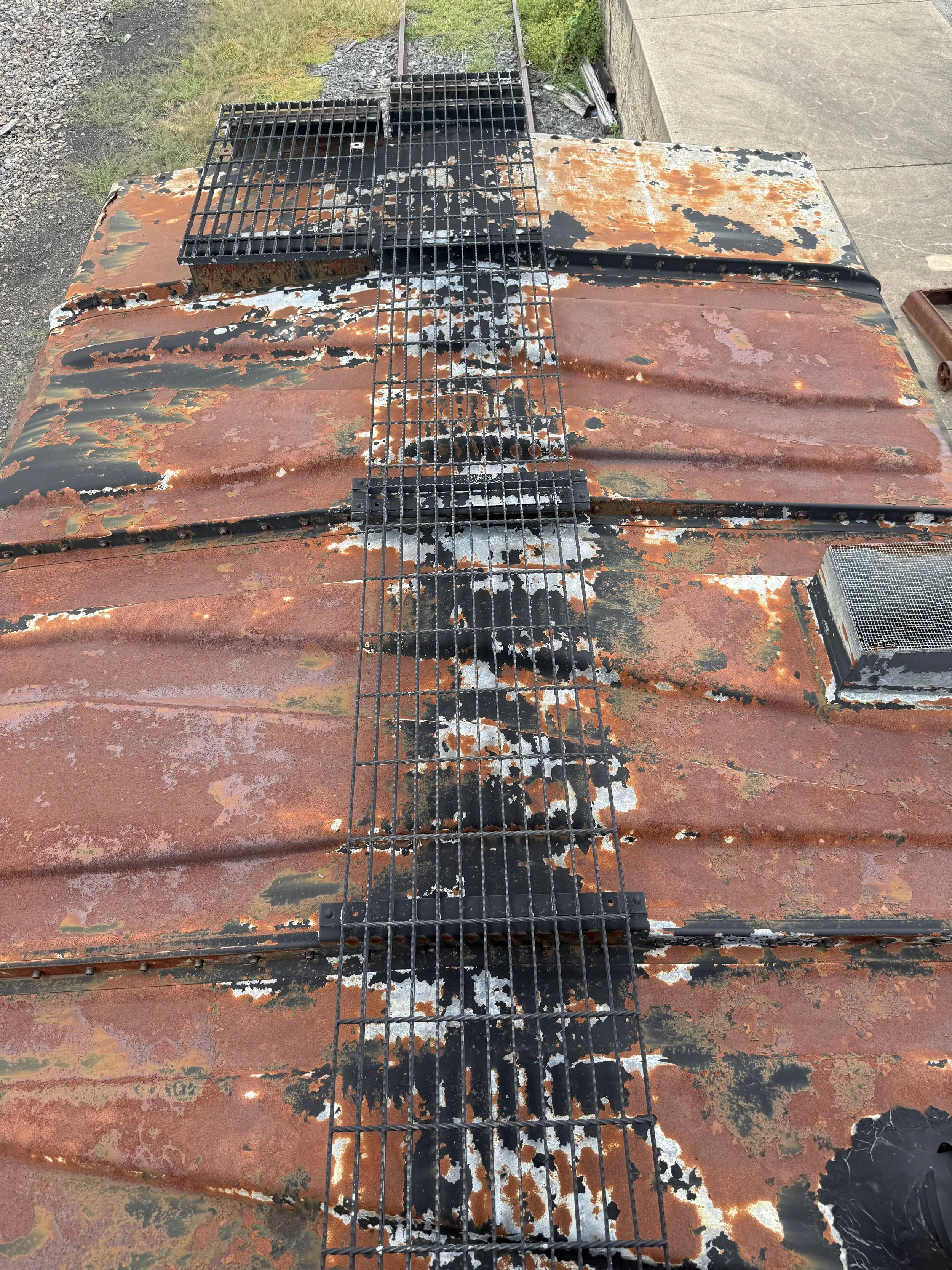 Rusty, weathered metal surface with black and white peeling paint, and a metal grid or grate running along the center.