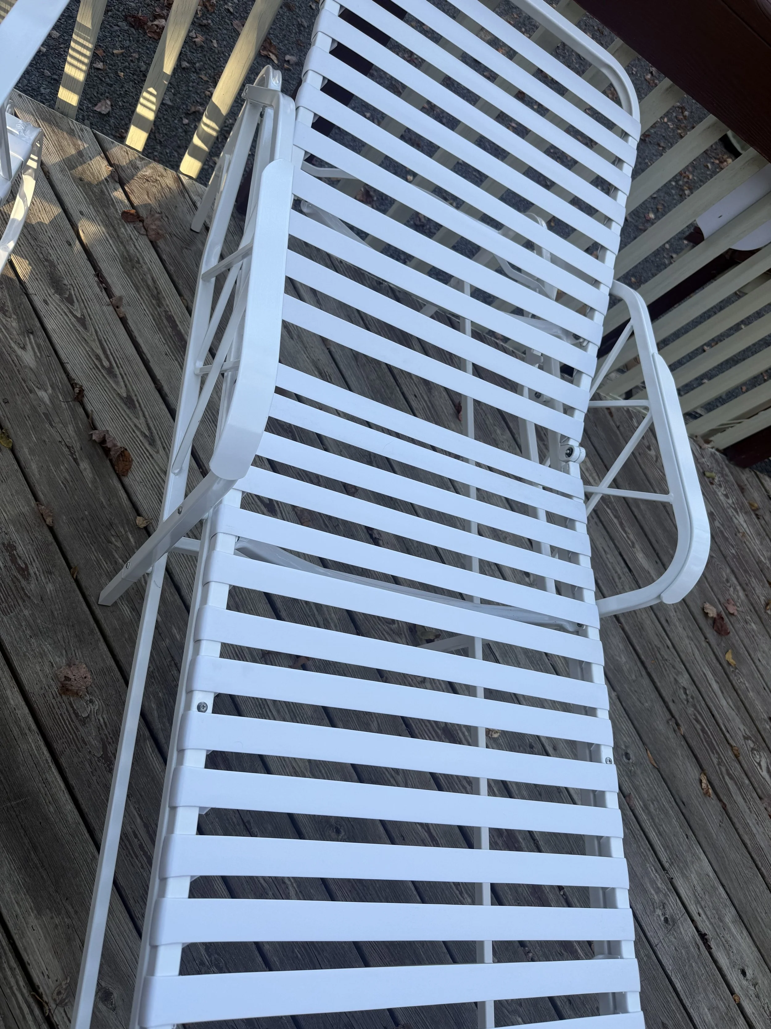 White metal outdoor lounge chair on wooden deck with scattered leaves.