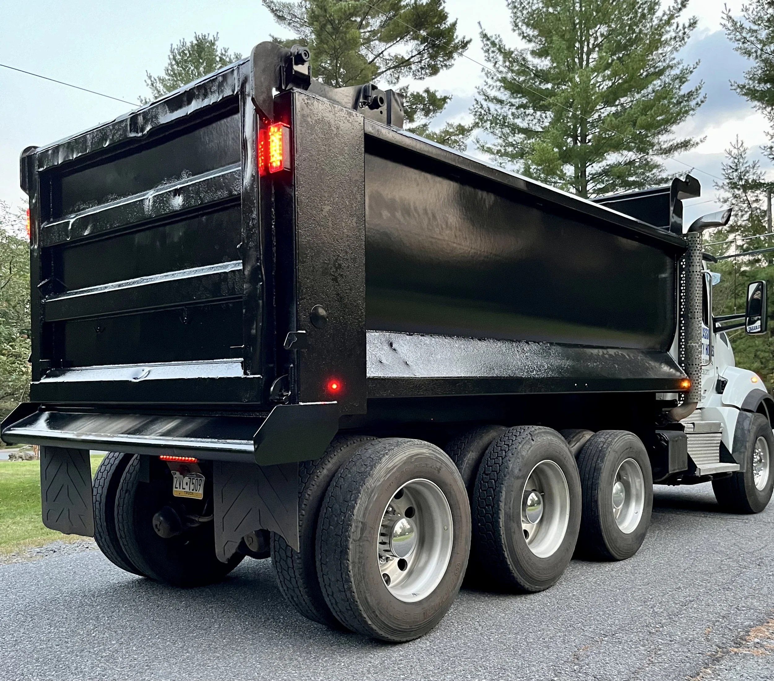 A black dump truck parked on a paved road with green grass and trees in the background.