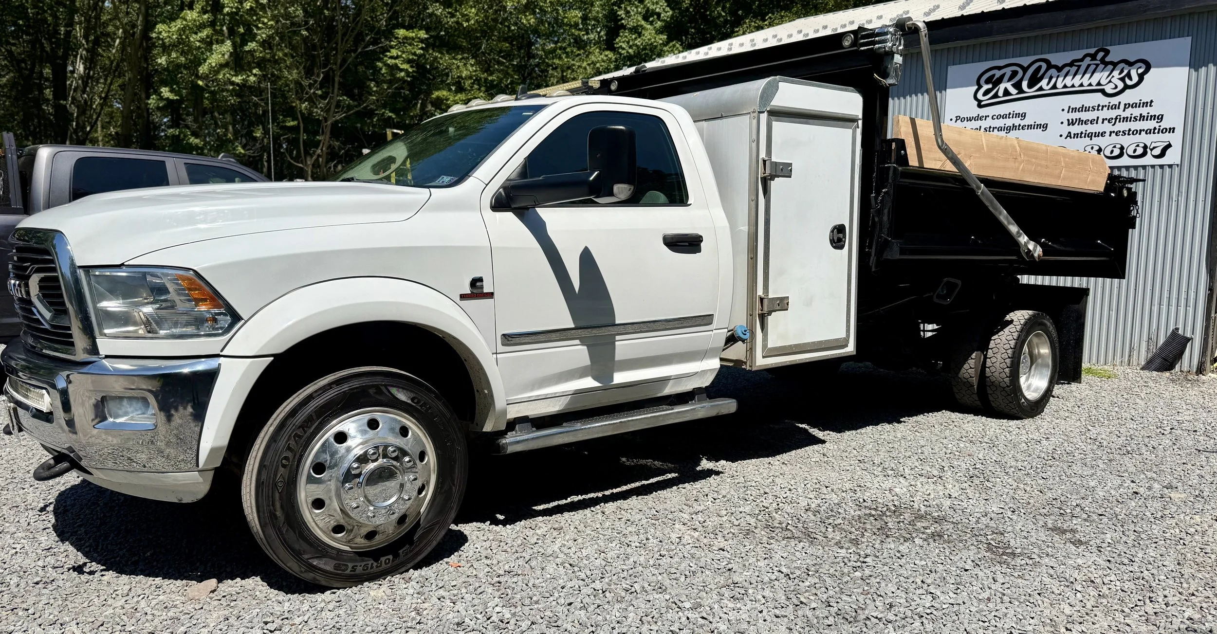 White utility truck with a black flatbed, parked on a gravel lot outside a building with a sign for ER Coatings.