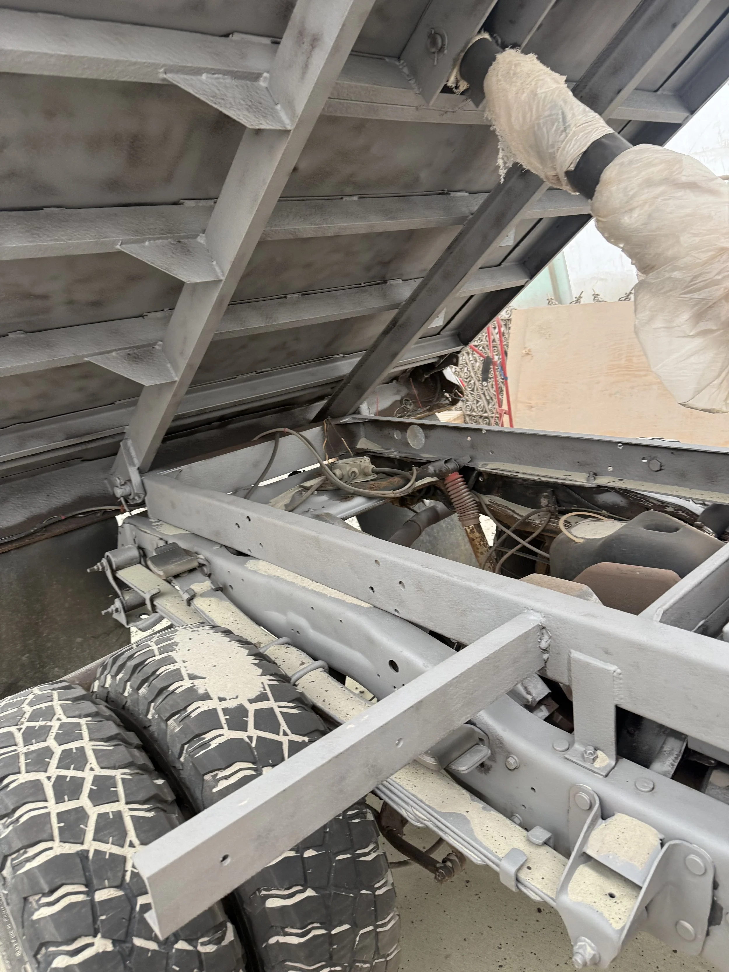 Close-up of a partially assembled or repaired vehicle chassis with tires, metal framework, wiring, and an overhead bed or cargo bed.