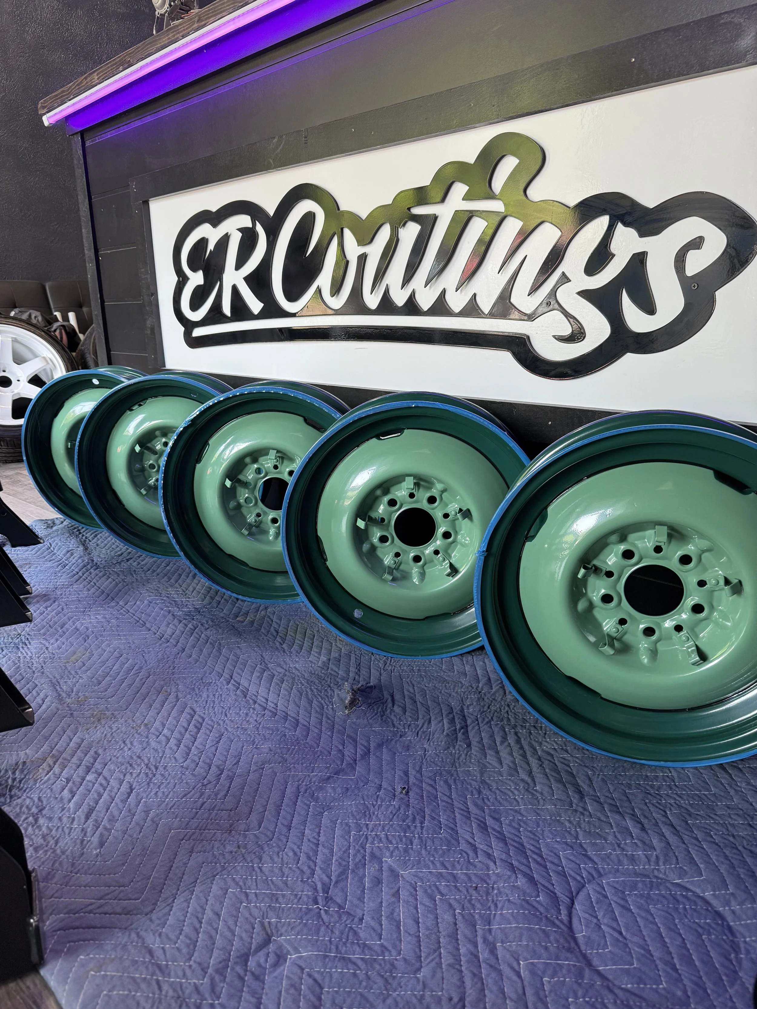 Four green car wheels placed in a row on a blue padded surface, with a sign that says "GROUTN'S" in the background.