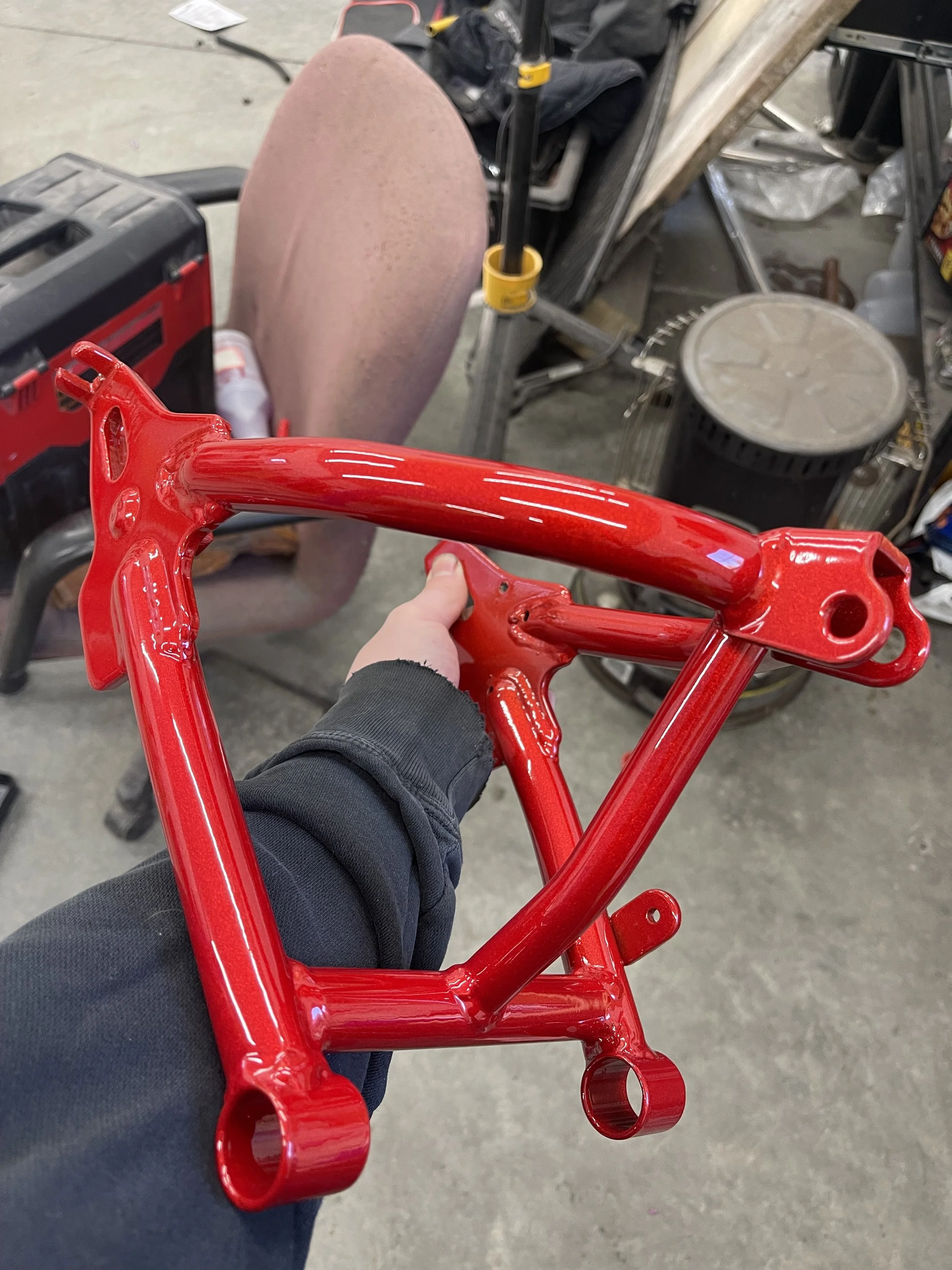 A person holding a freshly painted red bicycle frame inside a workshop or garage.