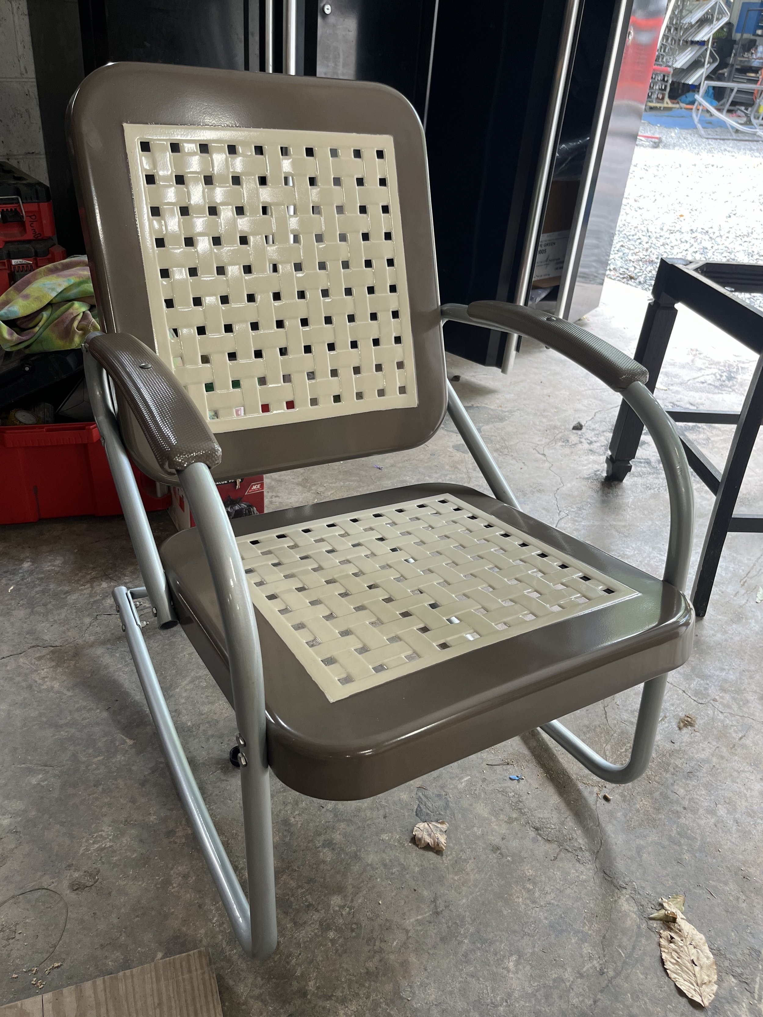 A tan and beige patio chair with a woven plastic seat and backrest frame, located indoors on a concrete floor.