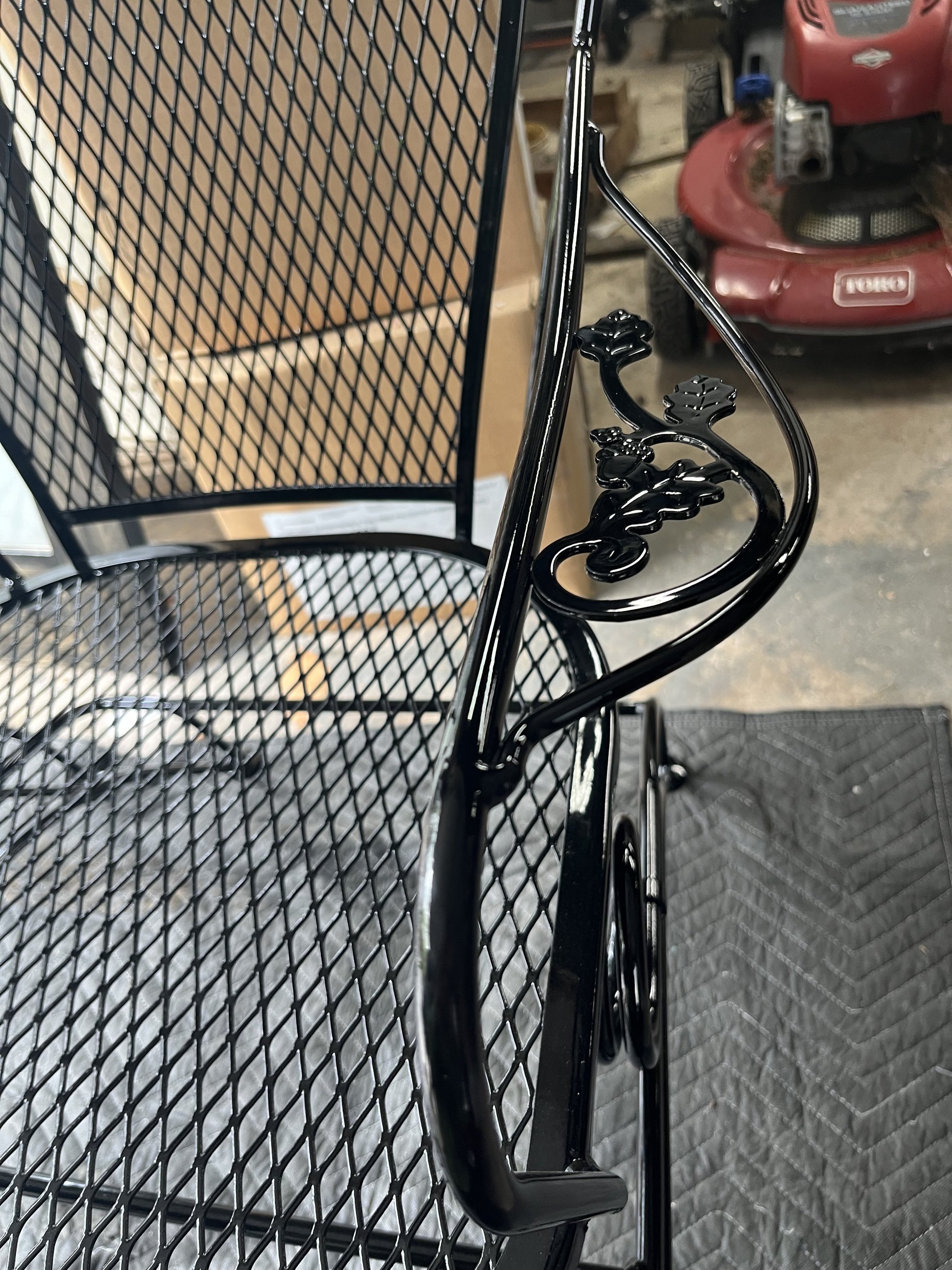 Black outdoor metal table and chair with decorative floral design on the armrest in a workshop or garage area.