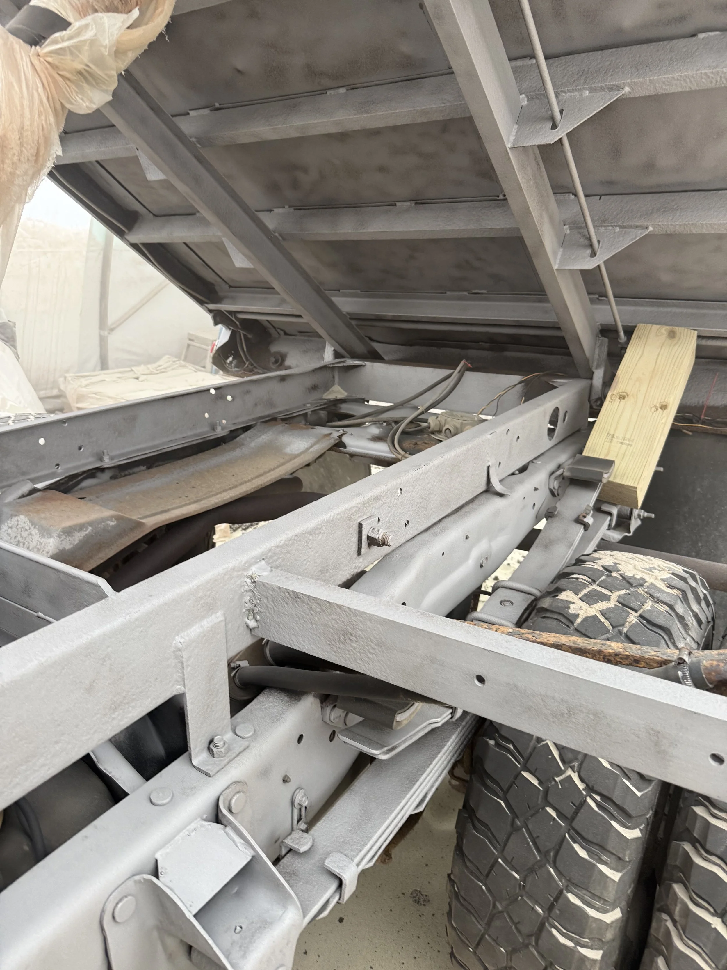 Close-up of a vehicle chassis with tires, metal frame, and hydraulic components, with the truck bed lifted.