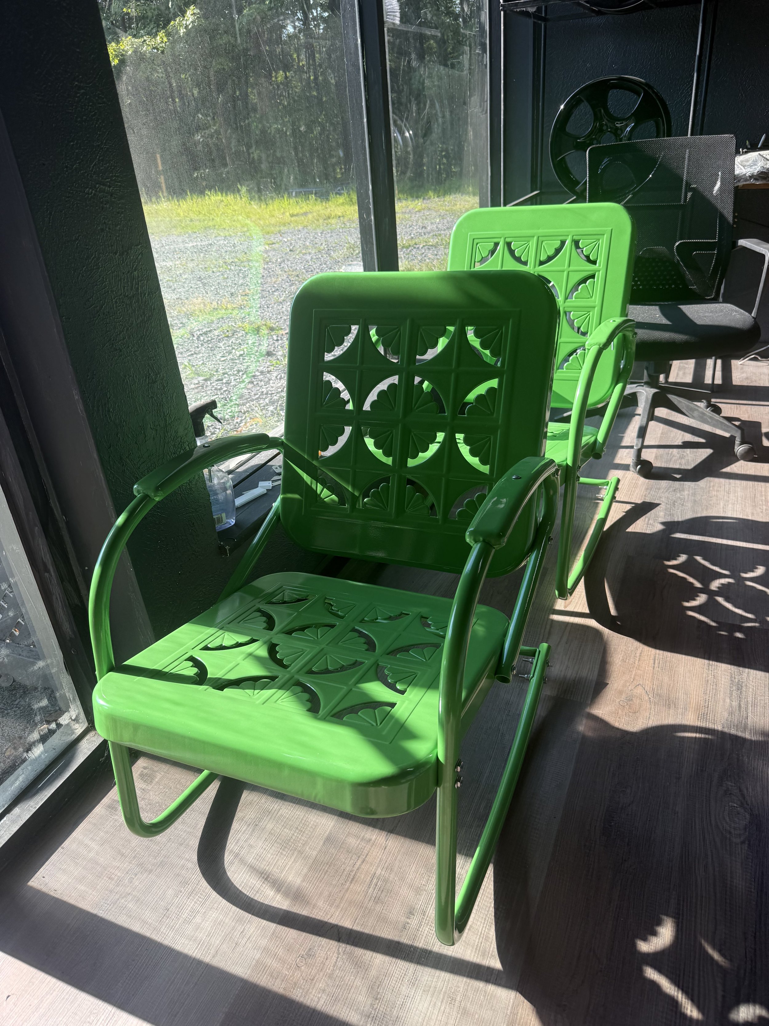 Green patterned chairs with armrests arranged in a row inside a room with sunlight coming through large windows.