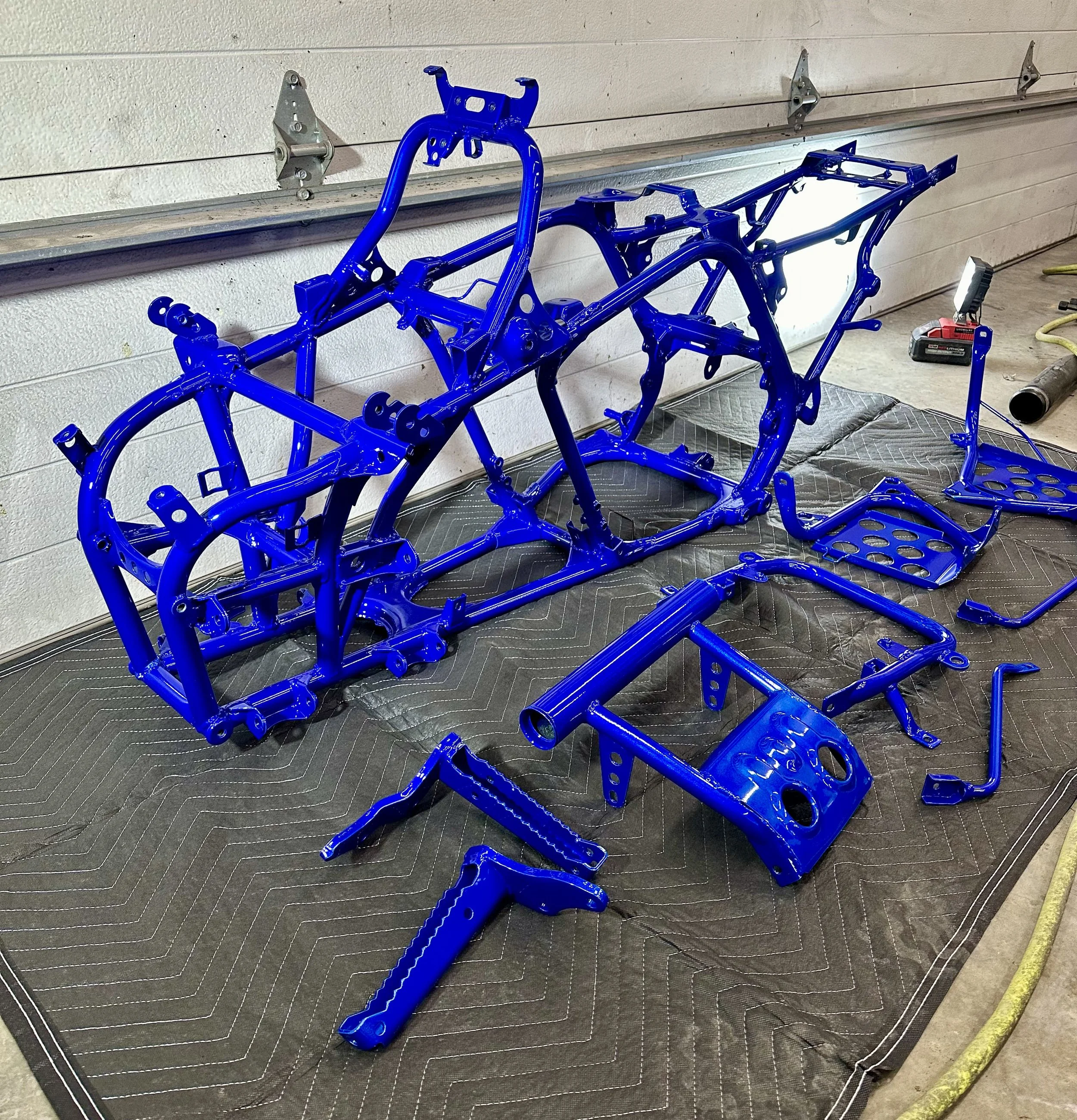 Blue motorcycle frame and parts laid out on a padded surface in a workshop.