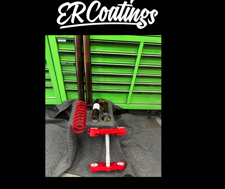 A set of motorcycle suspension parts, including two forks, a red coil spring, a red triple clamp, and some smaller components, placed on a black quilted fabric in front of a green tool chest with drawers labeled "ER Coatings."