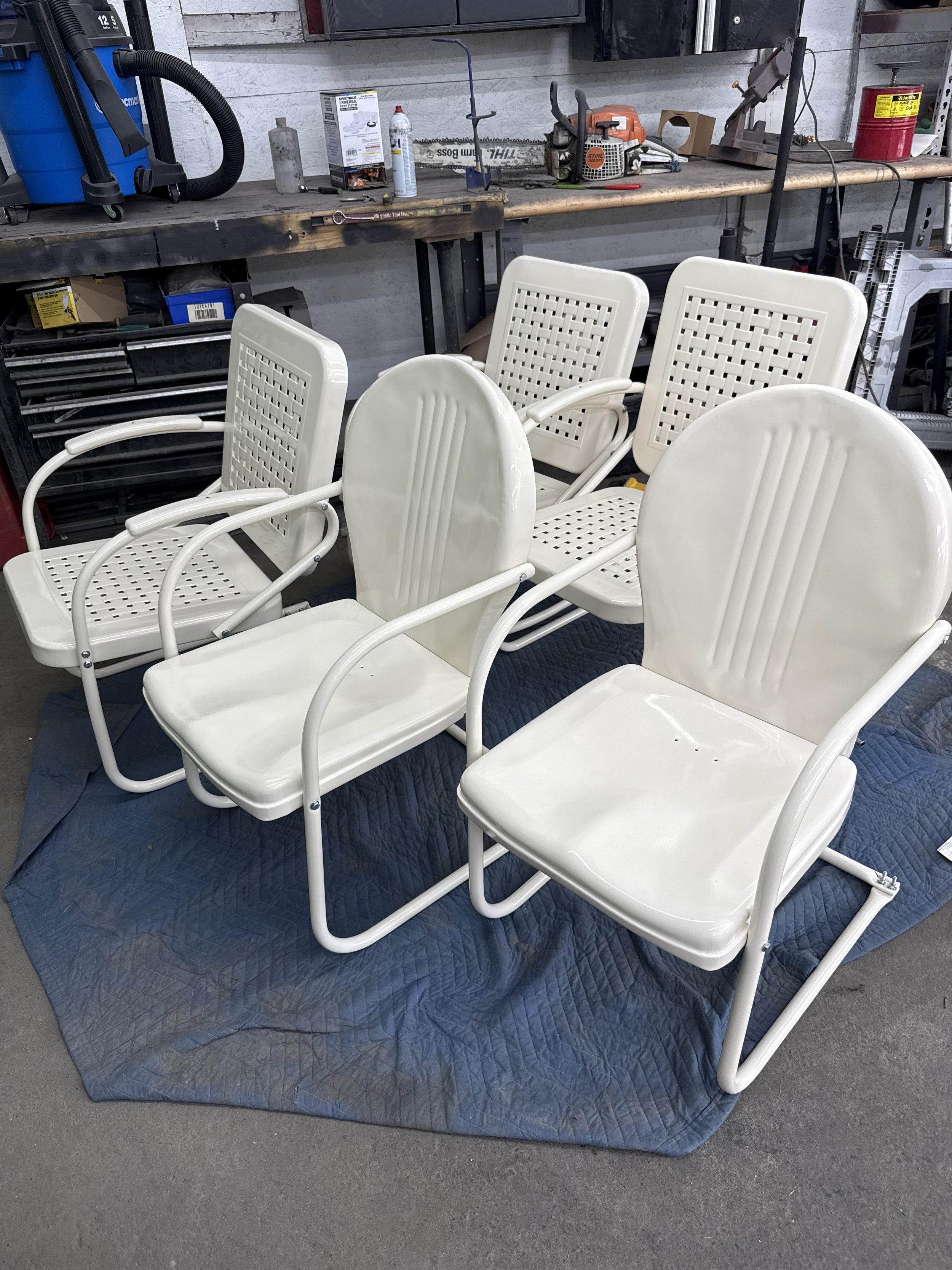 White plastic outdoor chairs with metal frames placed on a blue blanket in a workshop or garage setting.