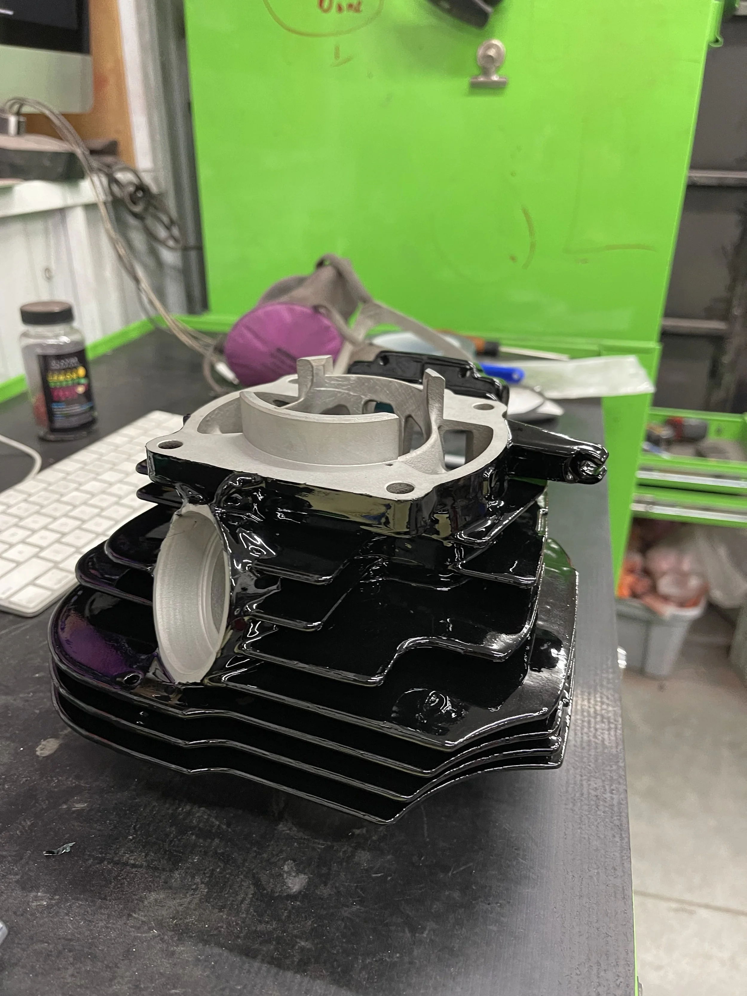 A black motorcycle engine cylinder with a silver piston on top, placed on a workbench in a workshop.