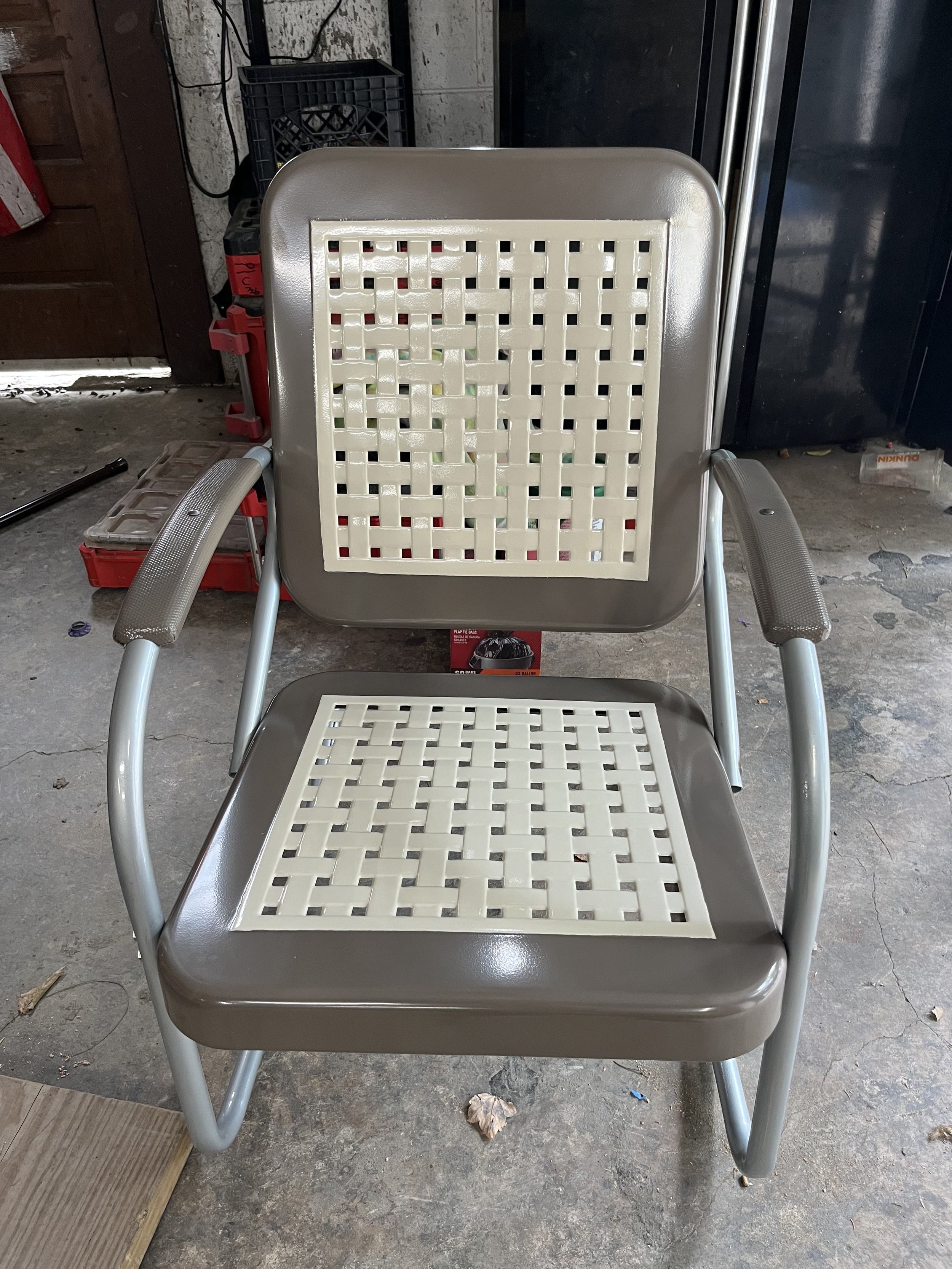A beige metal and plastic chair with a backrest and seat made of cream-colored lattice design. It is placed on a concrete floor in a garage or workshop.