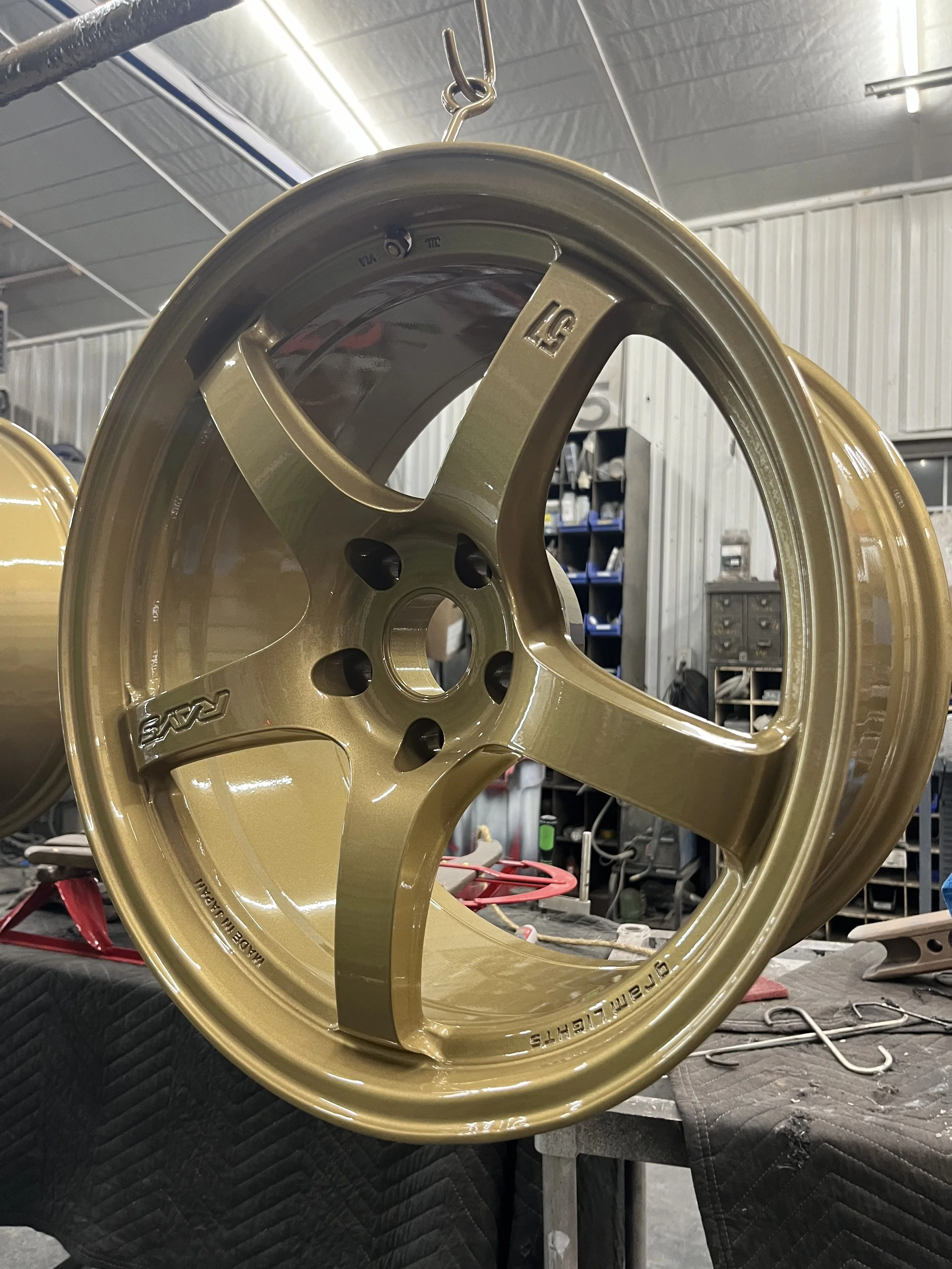 A gold-colored racing wheel rim hanging from a hook in a workshop.