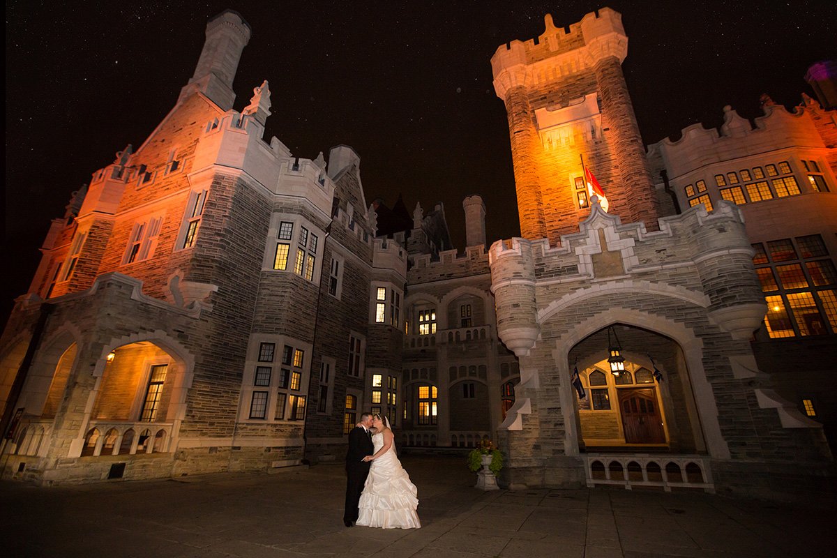 A bride and groom standing outside a large illuminated castle at night.