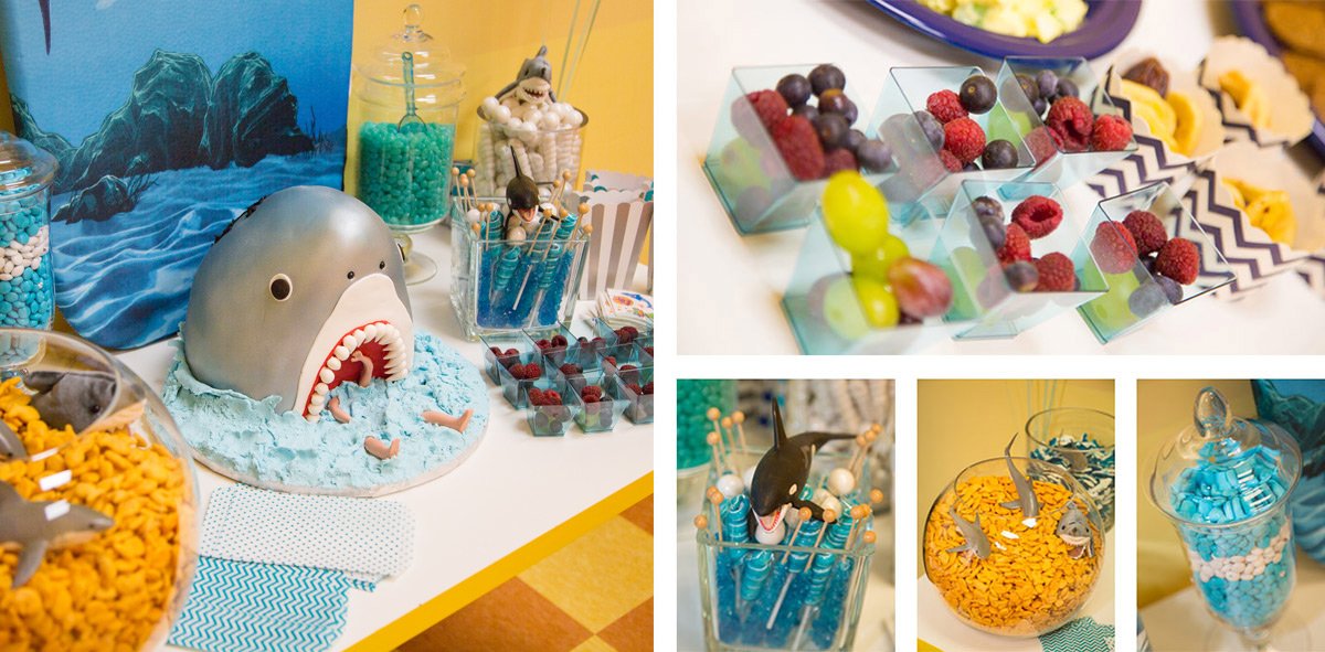 Dessert table decorated with a shark-themed cake, dinosaur-shaped lollipops, and various colorful candies and fruit treats.