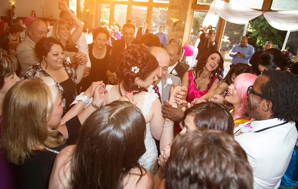 People dancing and celebrating at a wedding reception with sunlight streaming in.