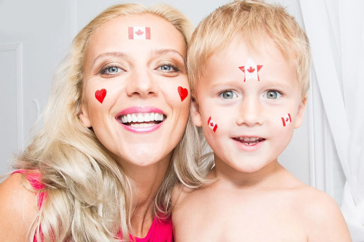 A woman and a young boy with Canadian flag face paint and stickers, smiling at the camera.