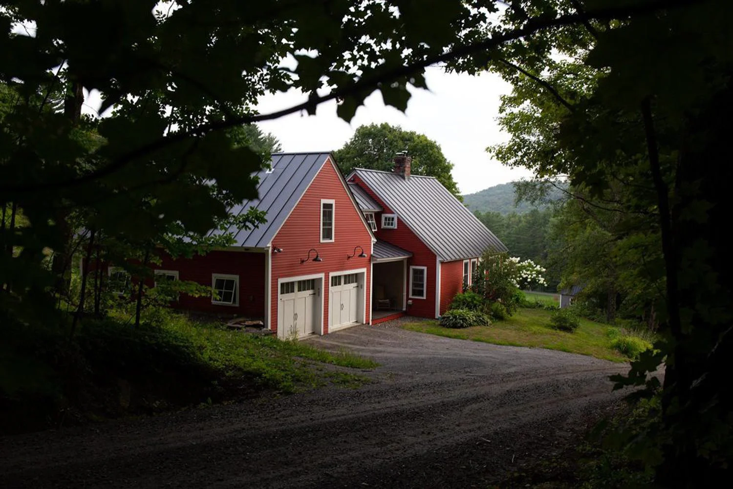 View through the trees of a red house with garage addition on a dirt road in Tunbridge, VT