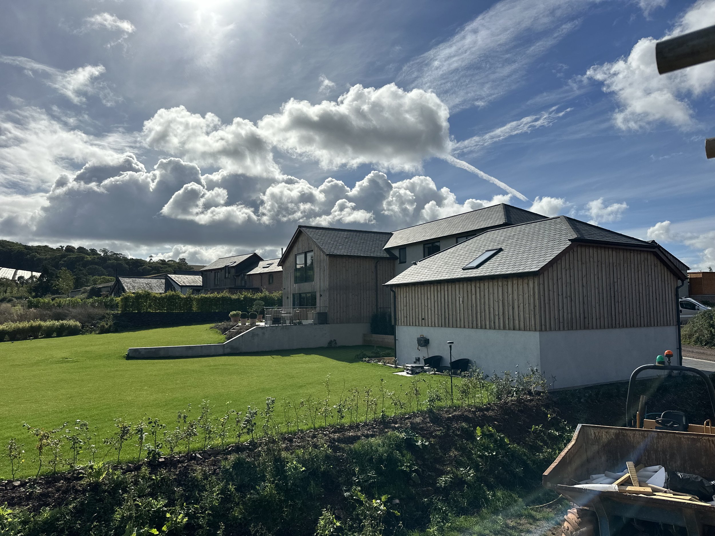 Modern house with a wooden exterior and sloped gray roof, surrounded by green lawn and garden, under a partly cloudy sky.