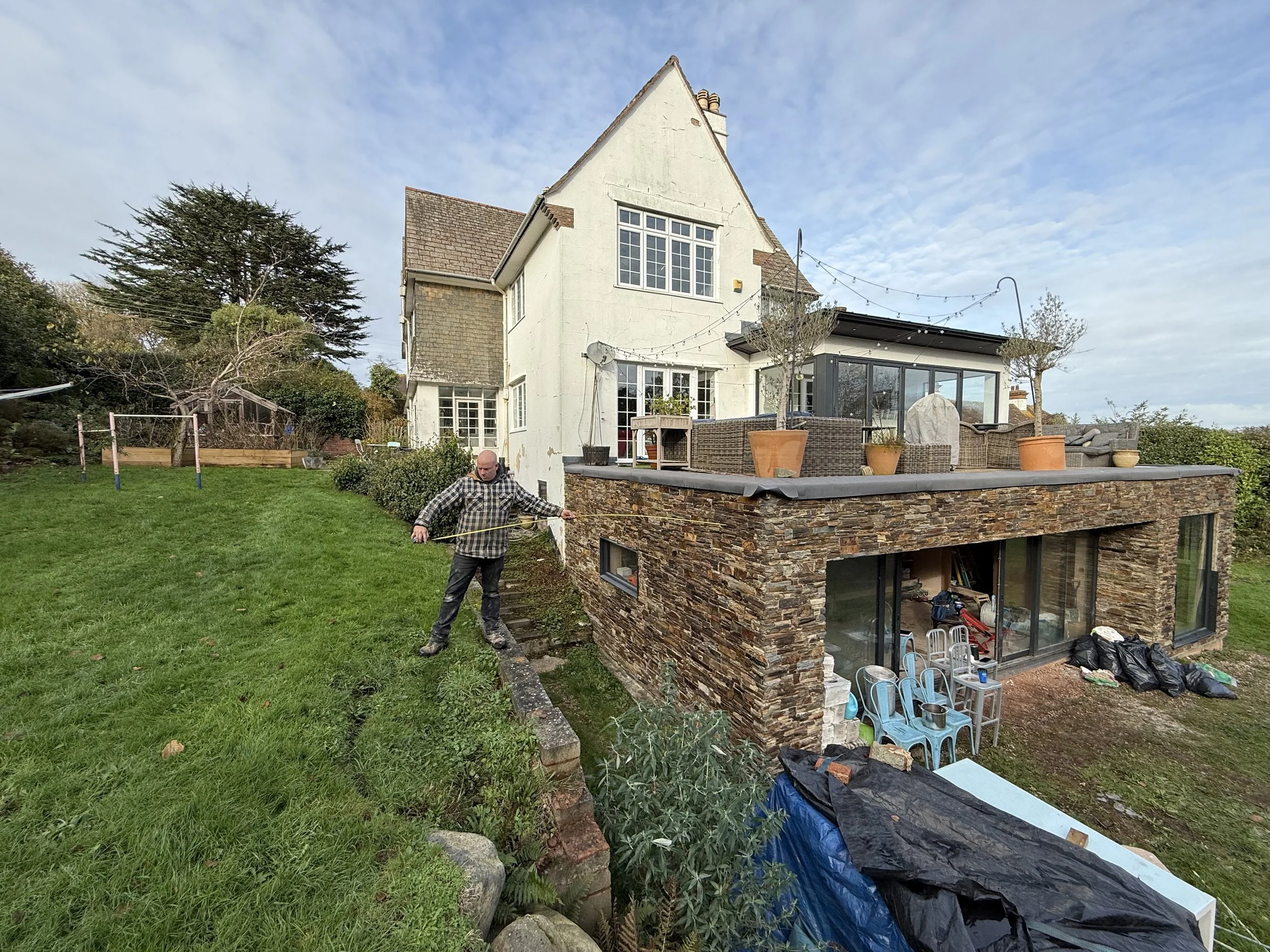 Man measuring a backyard with a house and patio in the background