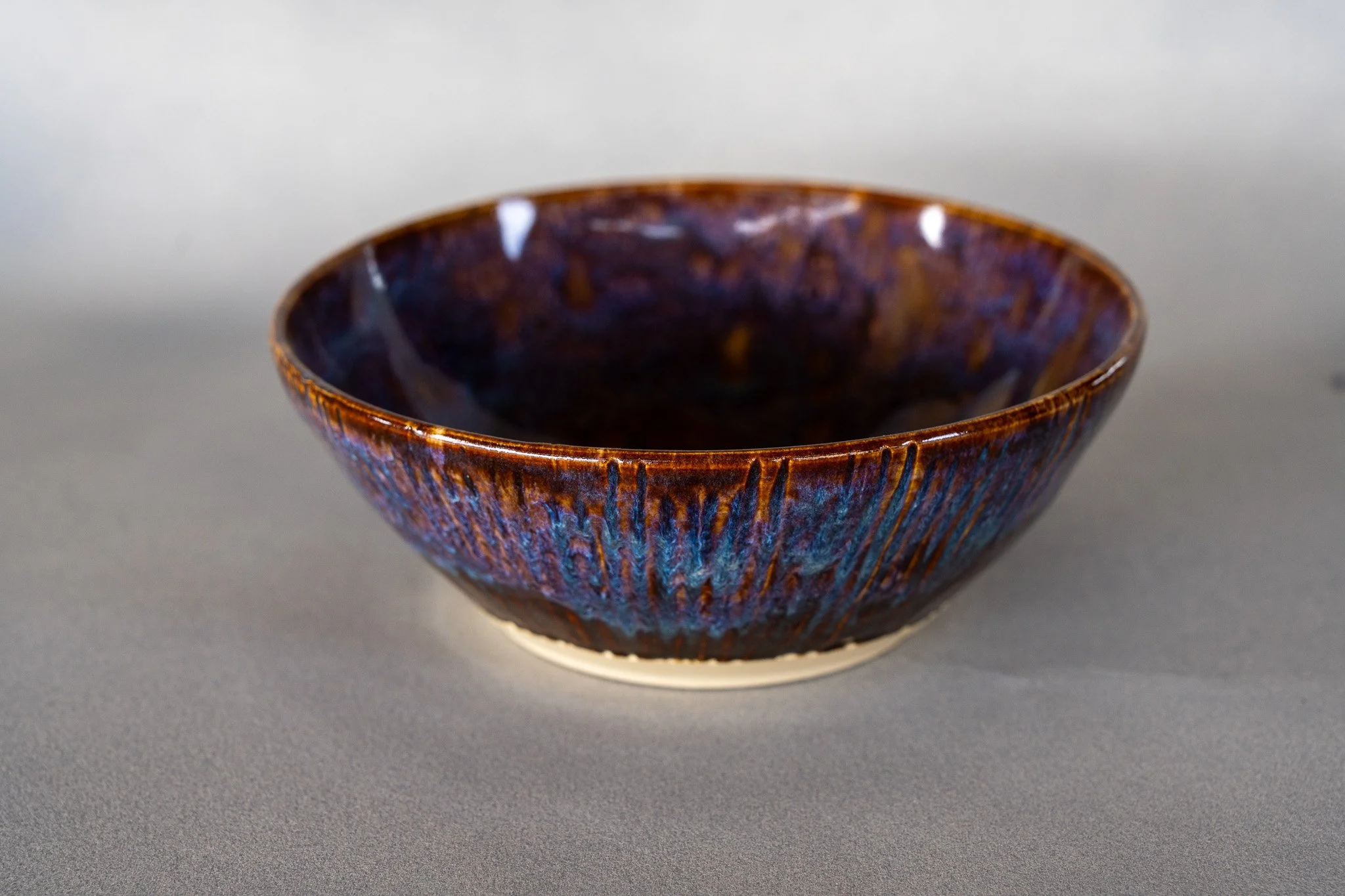 A ceramic bowl with a glossy, textured, dark brown and purple glaze, placed on a gray surface.