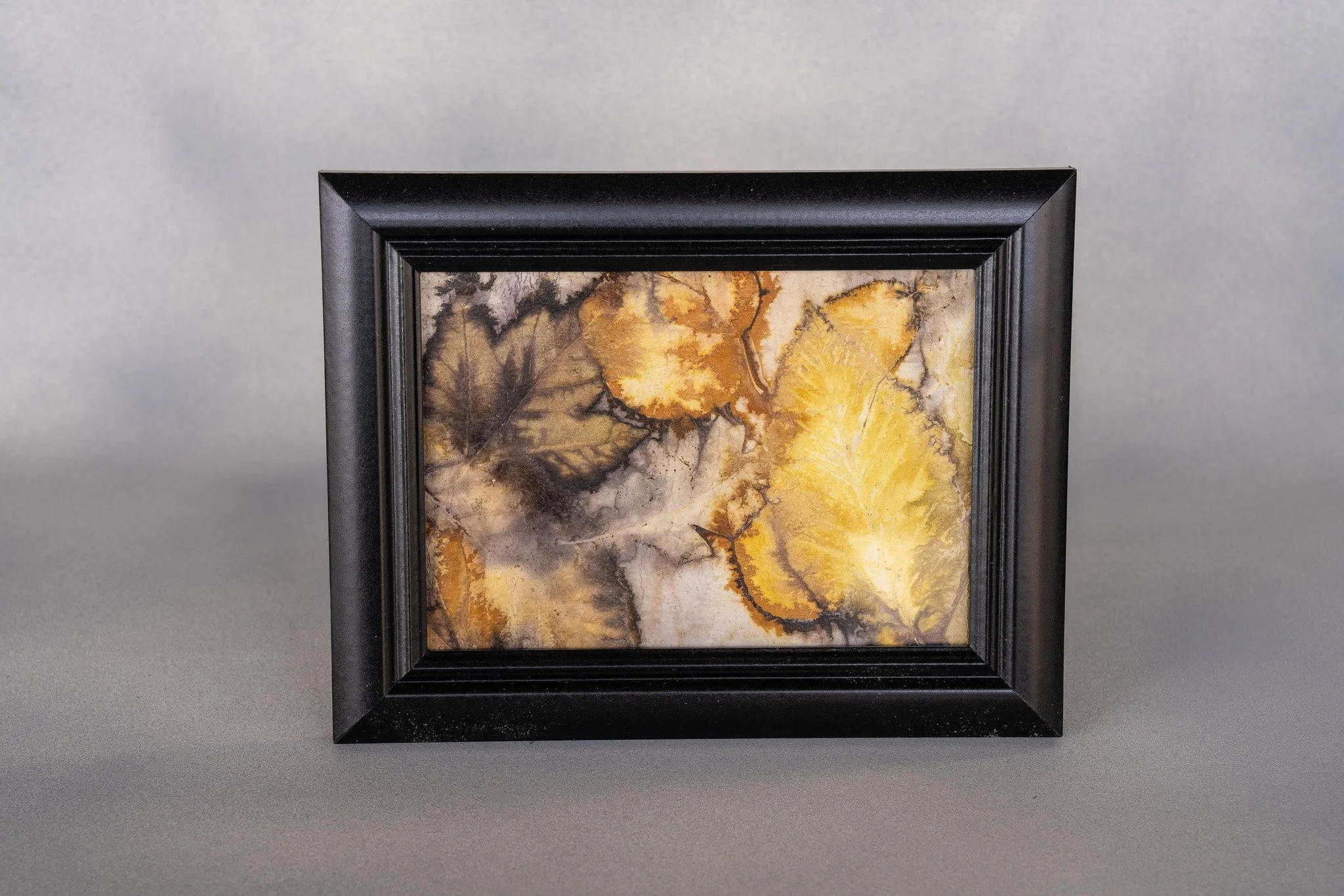 Framed watercolor painting of autumn leaves in shades of yellow, orange, brown, and black on a gray background.