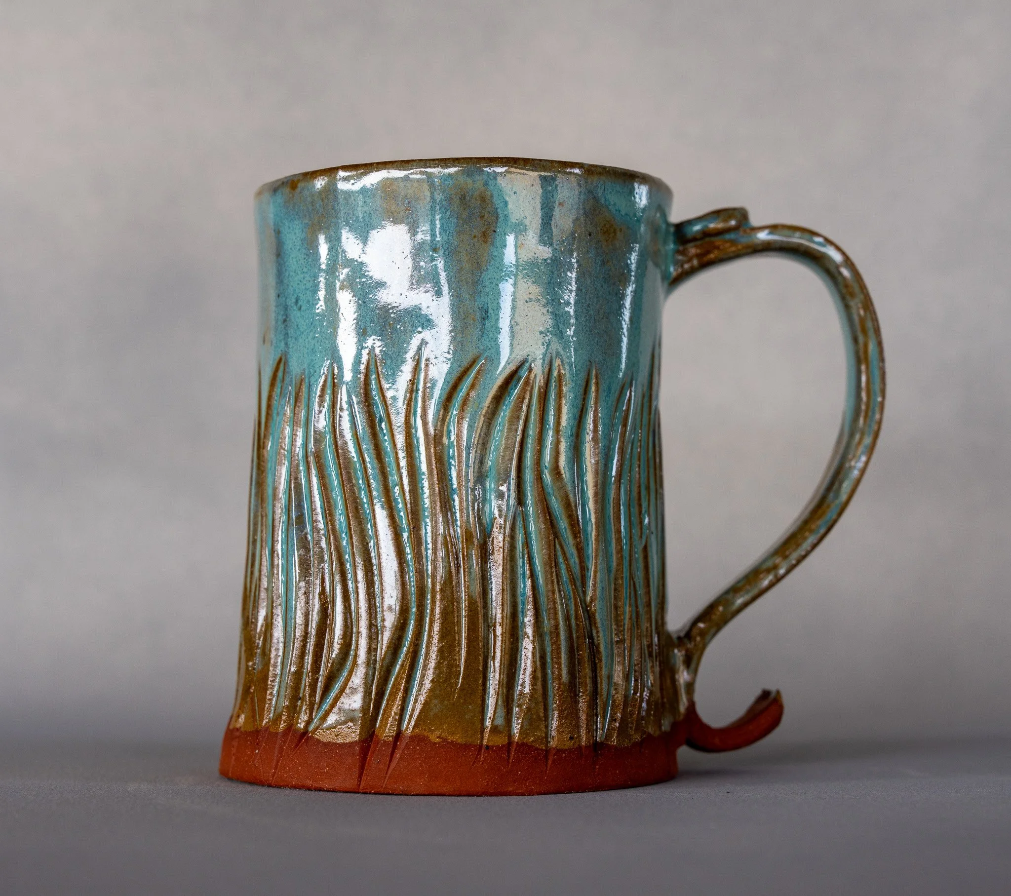 A ceramic mug with textured vertical lines and a wavy pattern, glazed in shades of blue, brown, and red.
