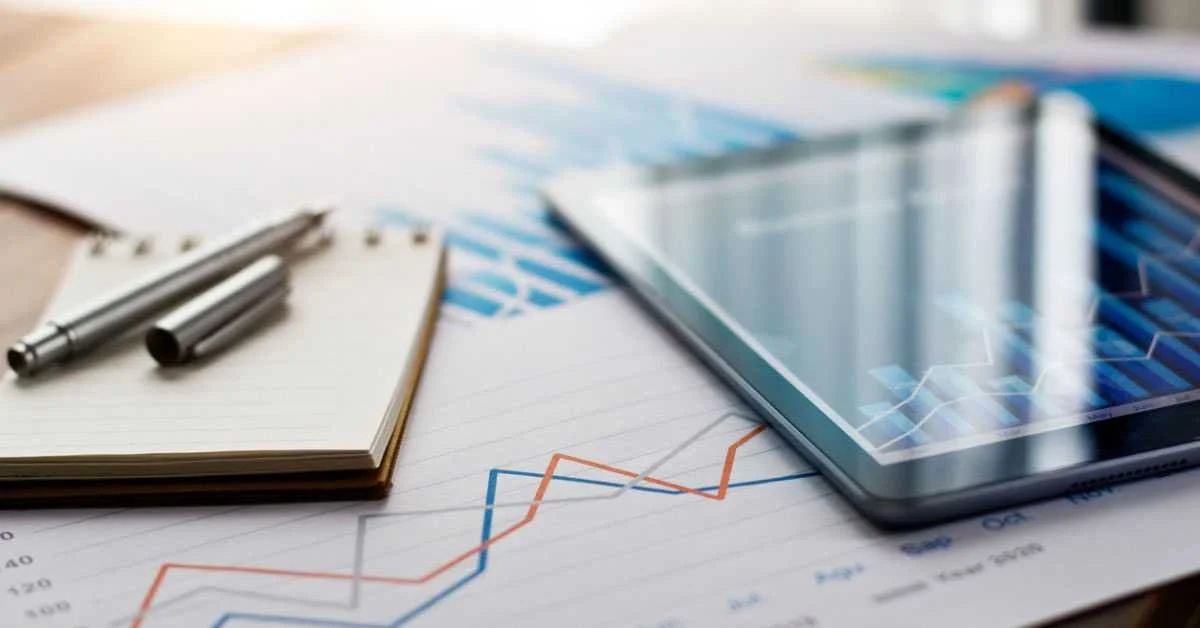 Business workspace with a tablet, notepad, pens, and financial graphs on paper.