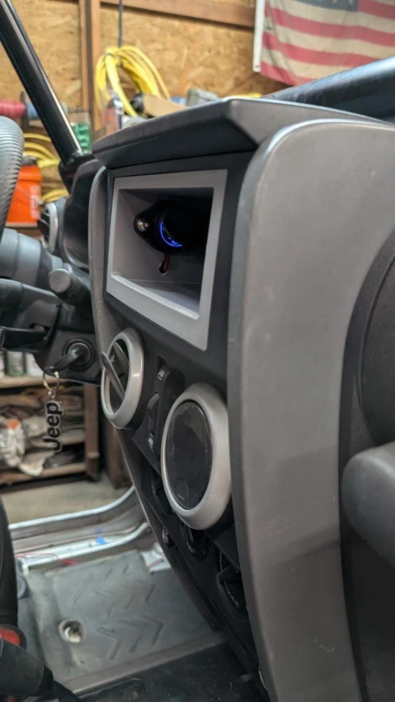Close-up view of a Jeep vehicle's dashboard with a focus on the center console, featuring two circular air vents, an empty slot or display, and a gear shifter to the left.