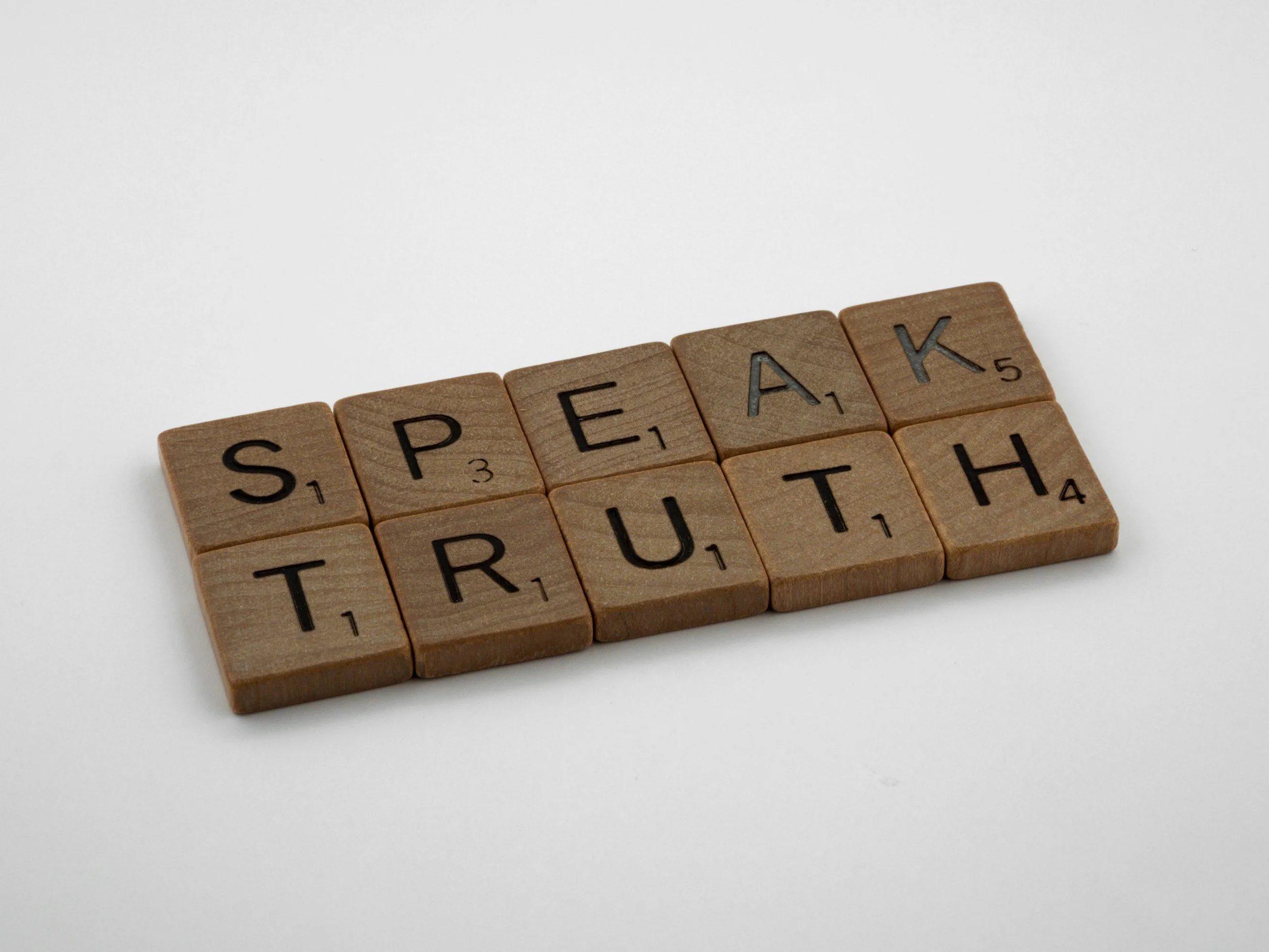 Wooden Scrabble tiles spelling the word 'SPEAK' on a white background.