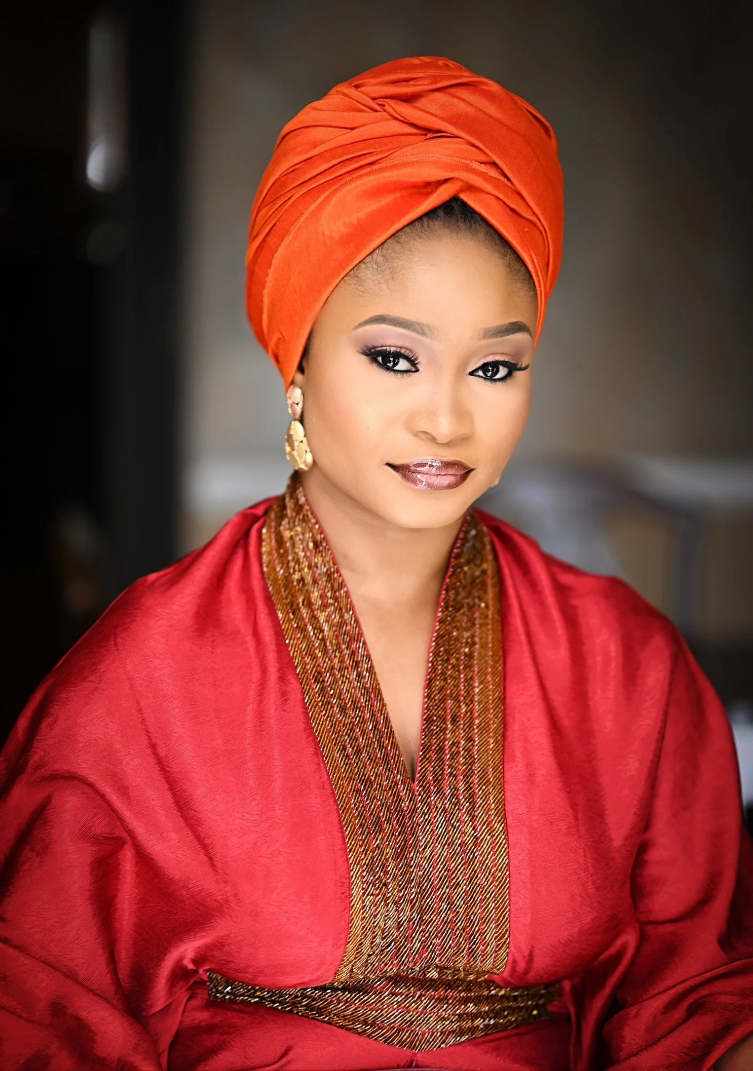 A woman dressed in a red satin traditional African attire and an orange headwrap.