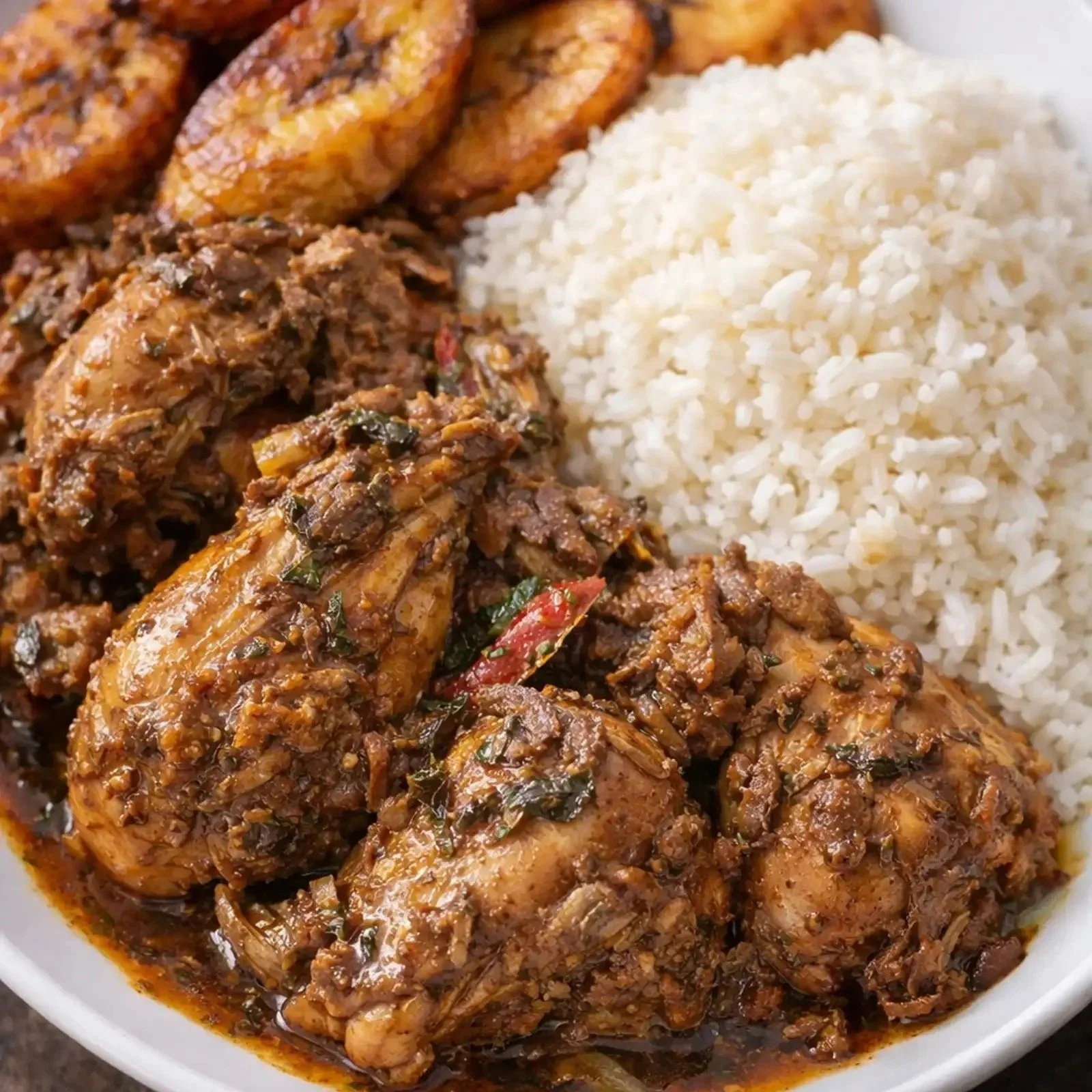 Plate of cooked chicken in spicy sauce, white rice, and plantains.