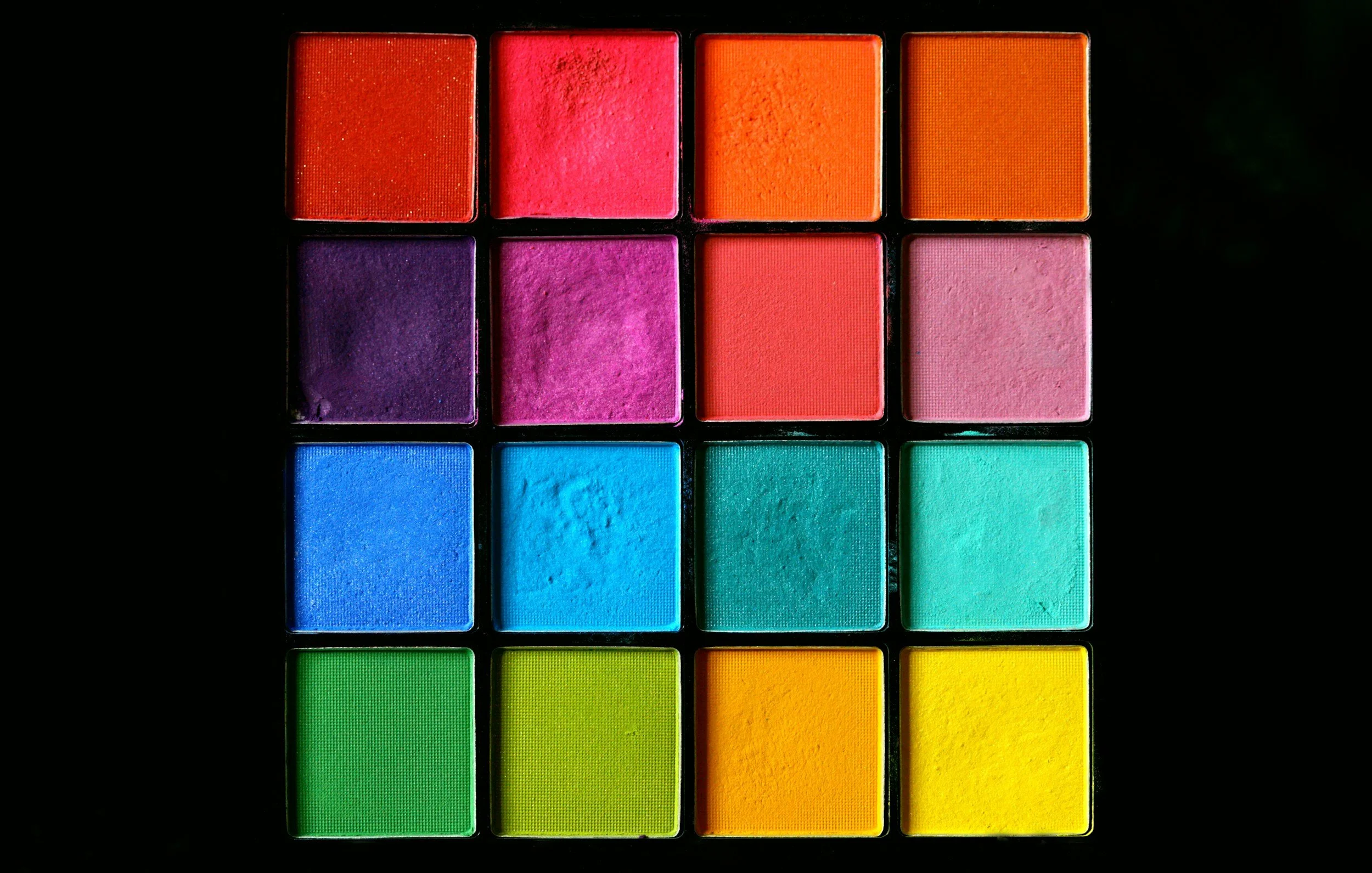 Colorful makeup eyeshadow palette with 16 shades arranged in a rectangular grid on a black background.