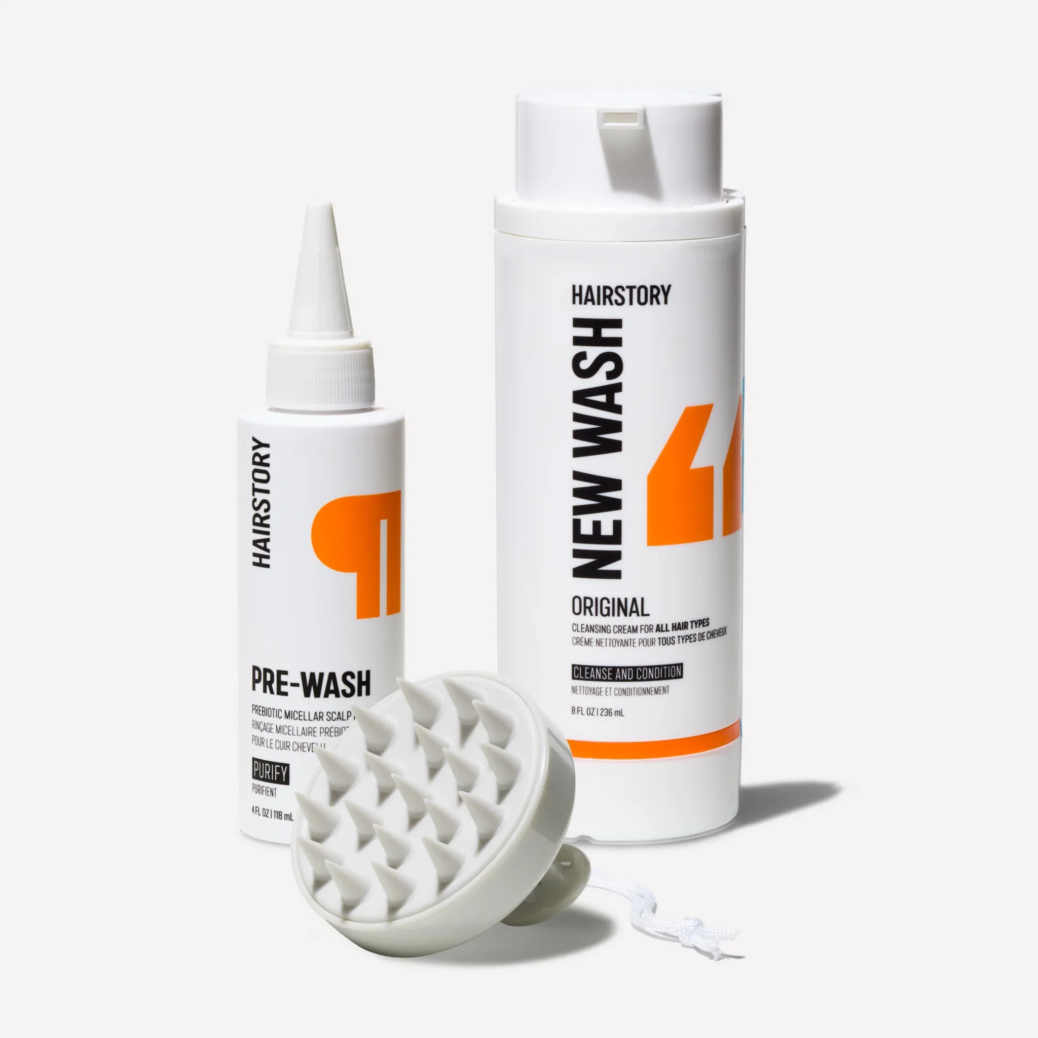Two bottles of hairstory hair care products, one labeled 'Pre-Wash' and the other 'Cleanse and Condition,' with a white cleaning brush in front.