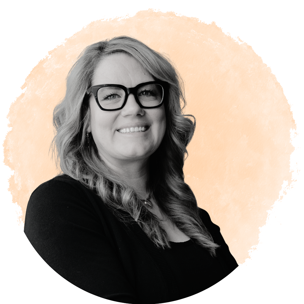 Black and white portrait of a woman with wavy hair, wearing glasses, smiling, against a peach-colored circular background.