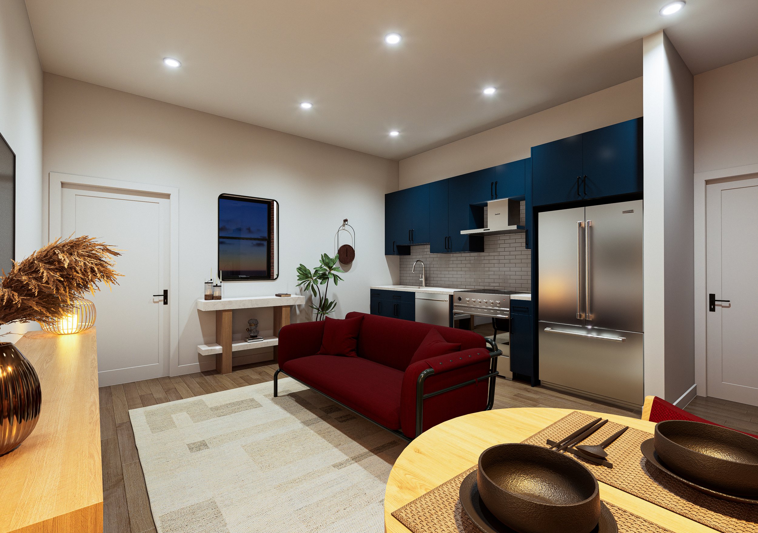 Interior view of a modern kitchen and living area with white walls, blue cabinetry, stainless steel appliances, a red sofa, a wooden dining table set with black bowls, and a window showing twilight outside.