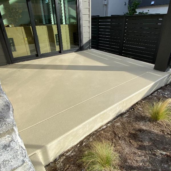 Newly poured concrete patio with a black fence and glass sliding door on a modern house exterior.